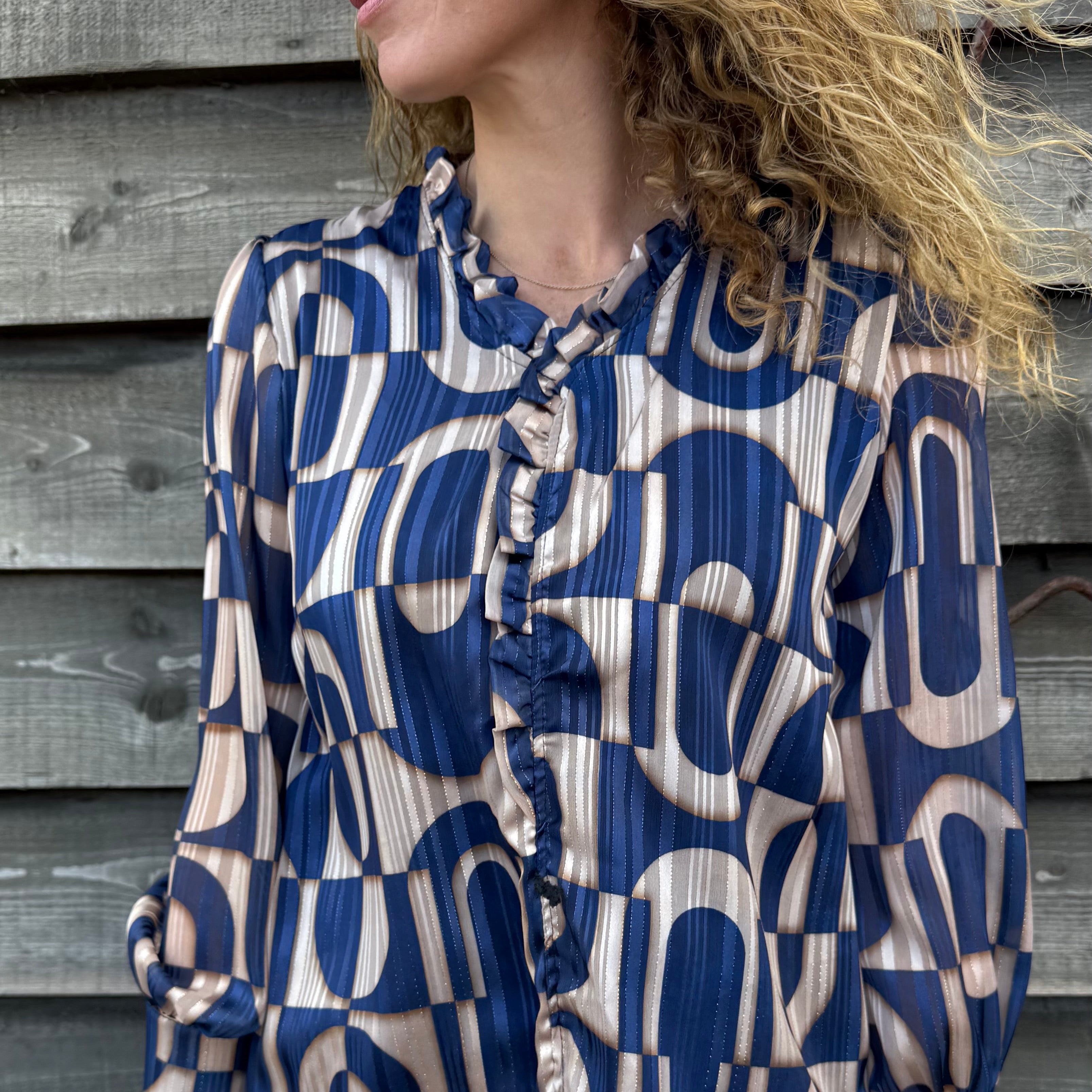 Woman wearing a blue and beige patterned blouse against a wooden wall.