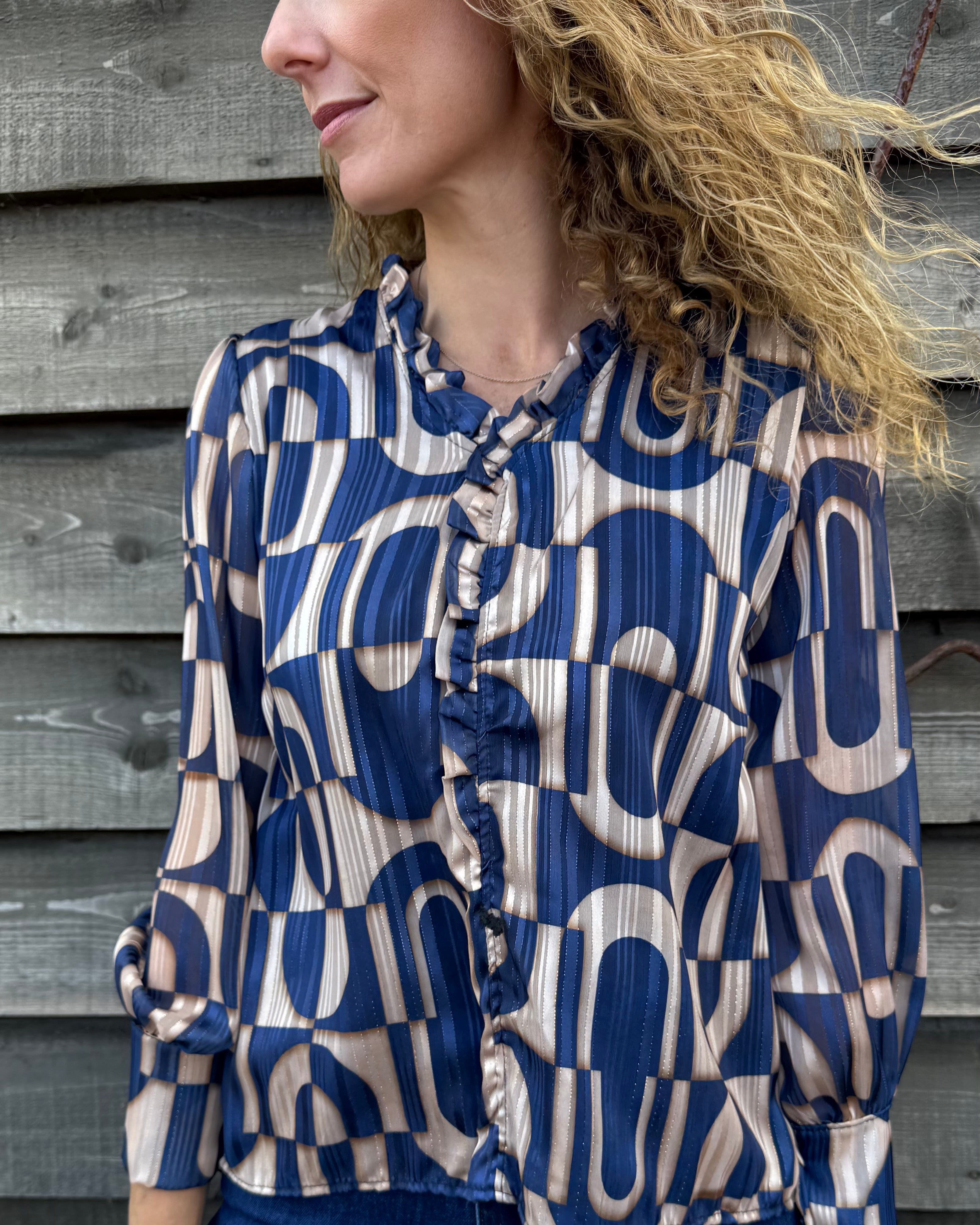 Woman wearing a blue and beige patterned blouse against a wooden wall.