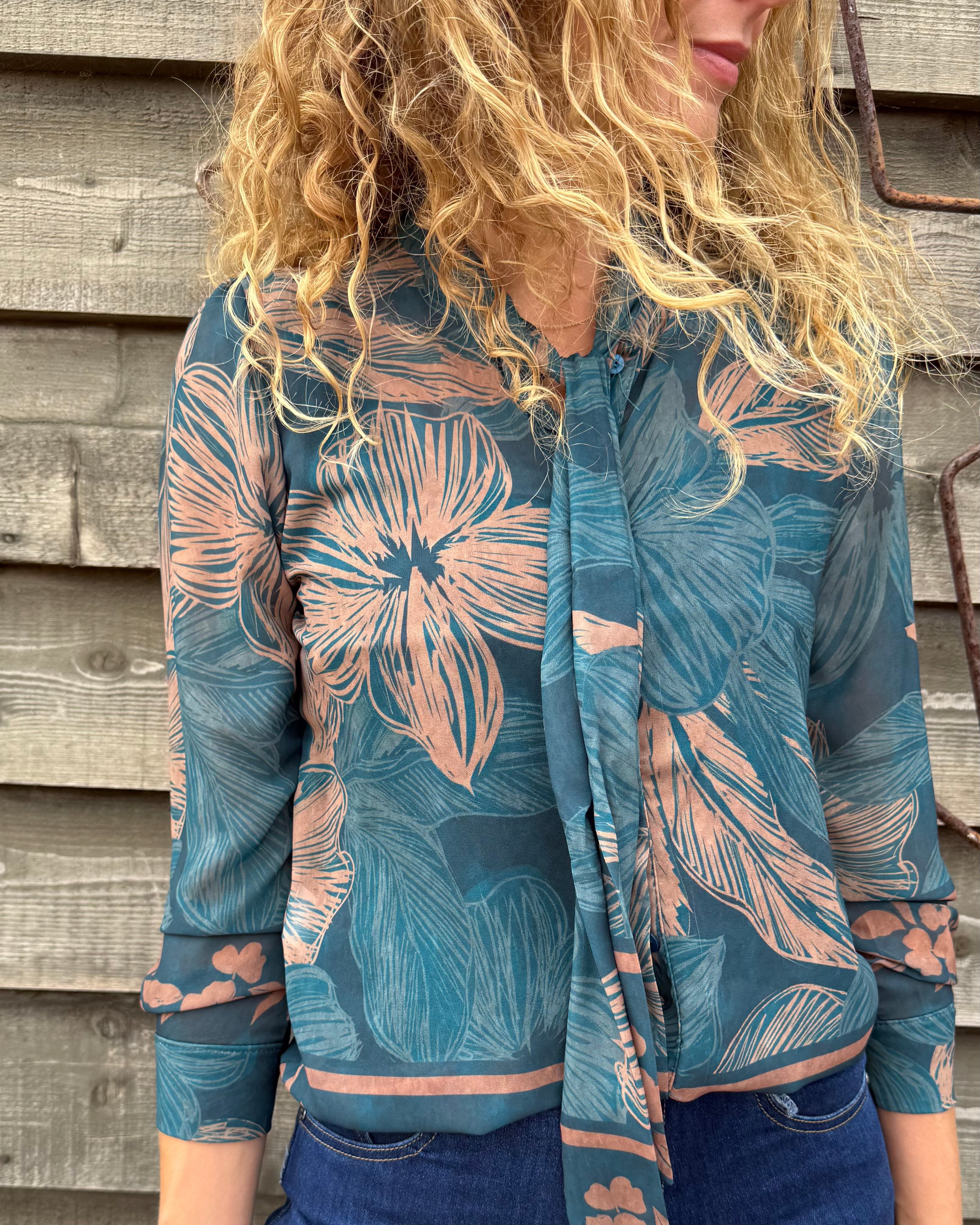 Person wearing a blue floral patterned shirt against a wooden wall.