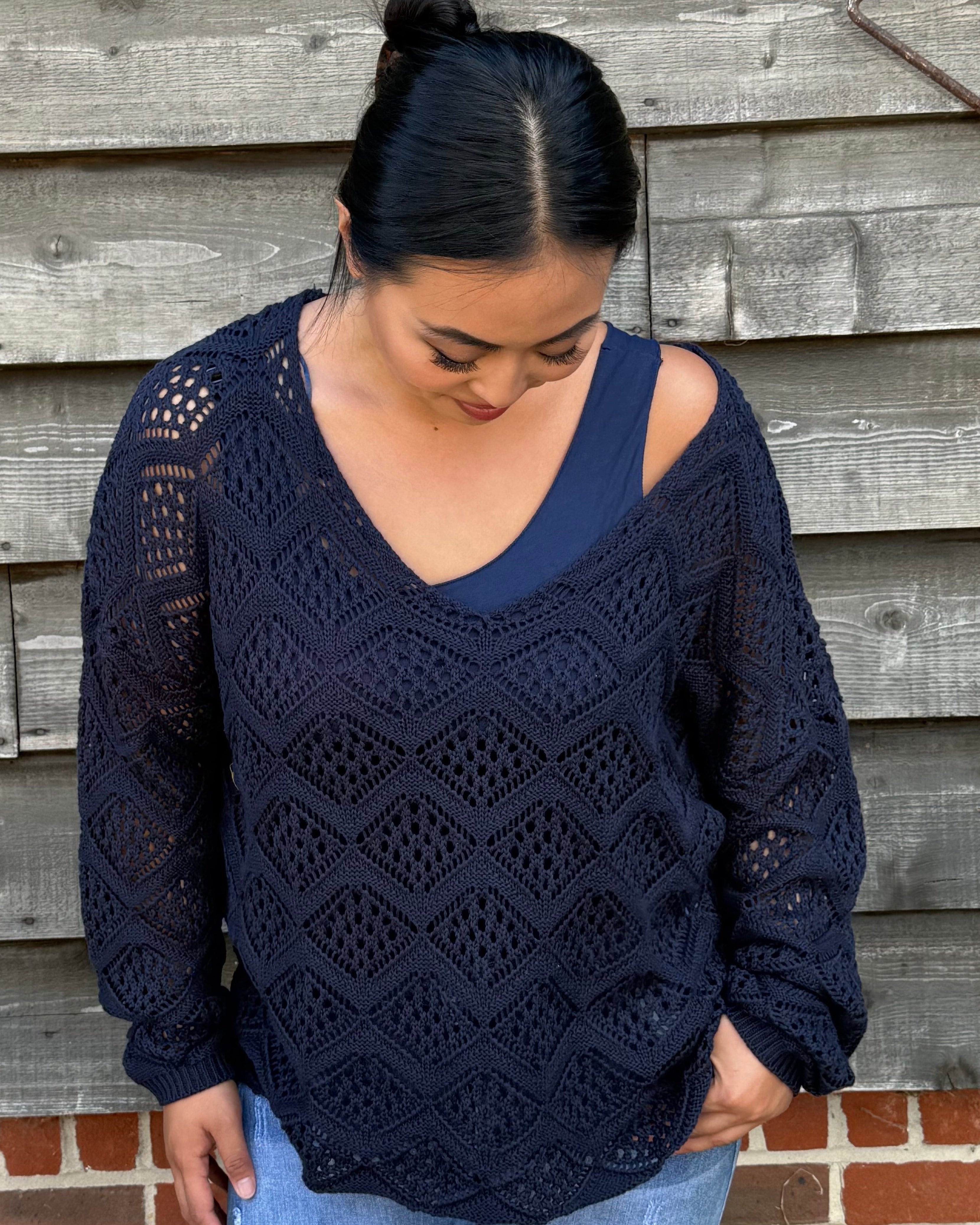 Woman wearing a navy blue lace sweater and denim shorts standing against a wooden wall.