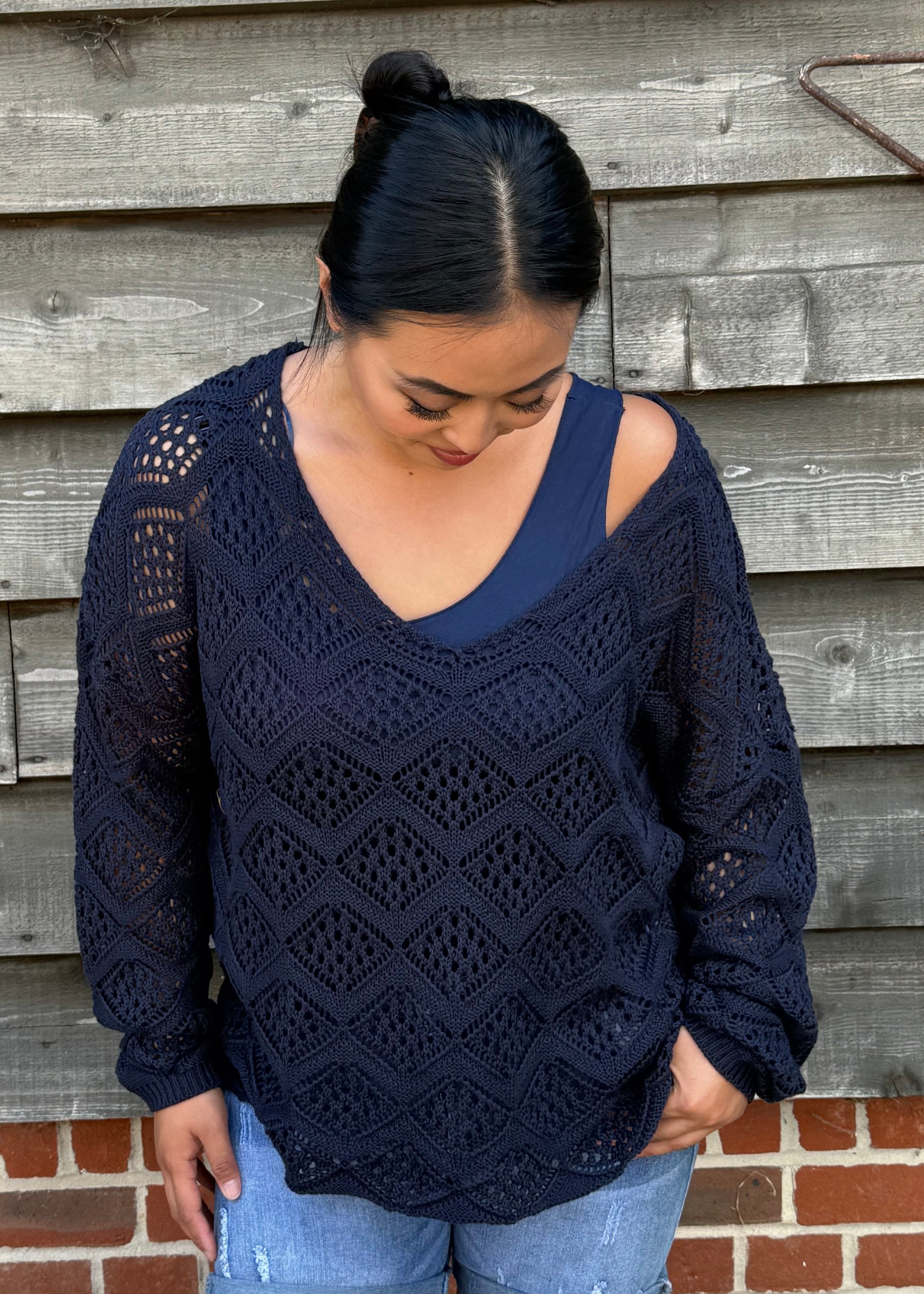 Woman wearing a navy blue lace sweater and denim shorts standing against a wooden wall.