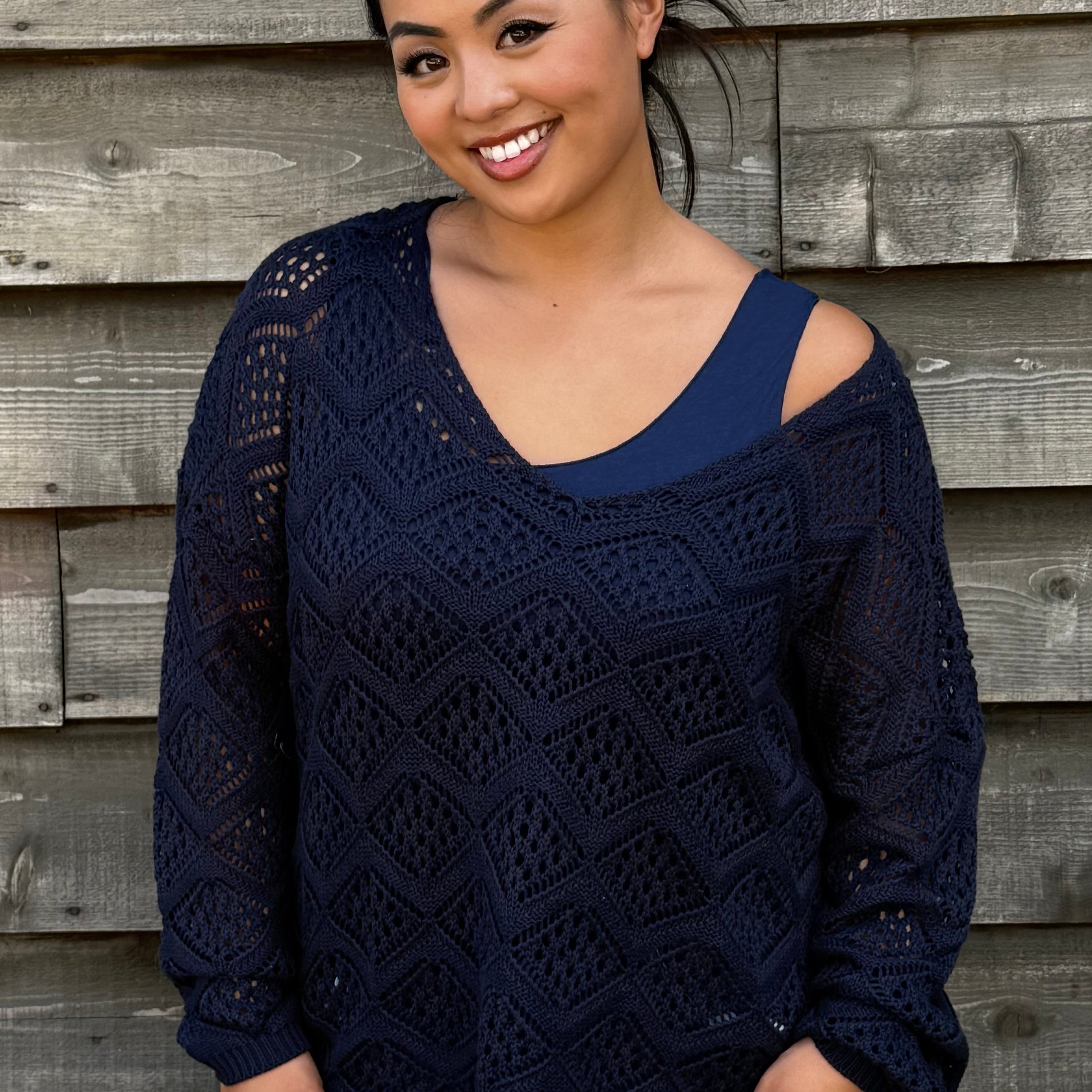Woman wearing a navy blue sweater with cut-out shoulders against a wooden wall.