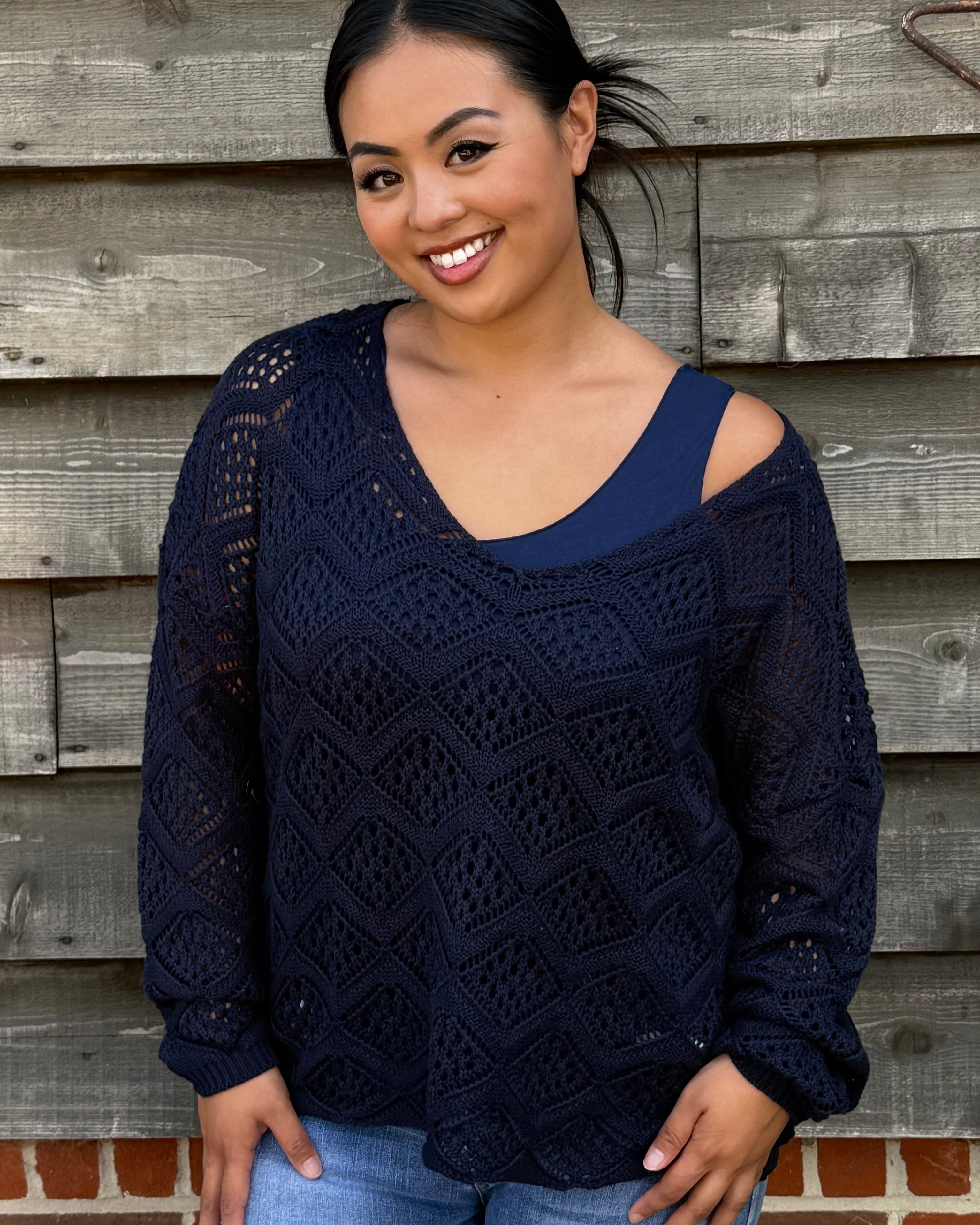 Woman wearing a navy blue sweater with cut-out shoulders against a wooden wall.