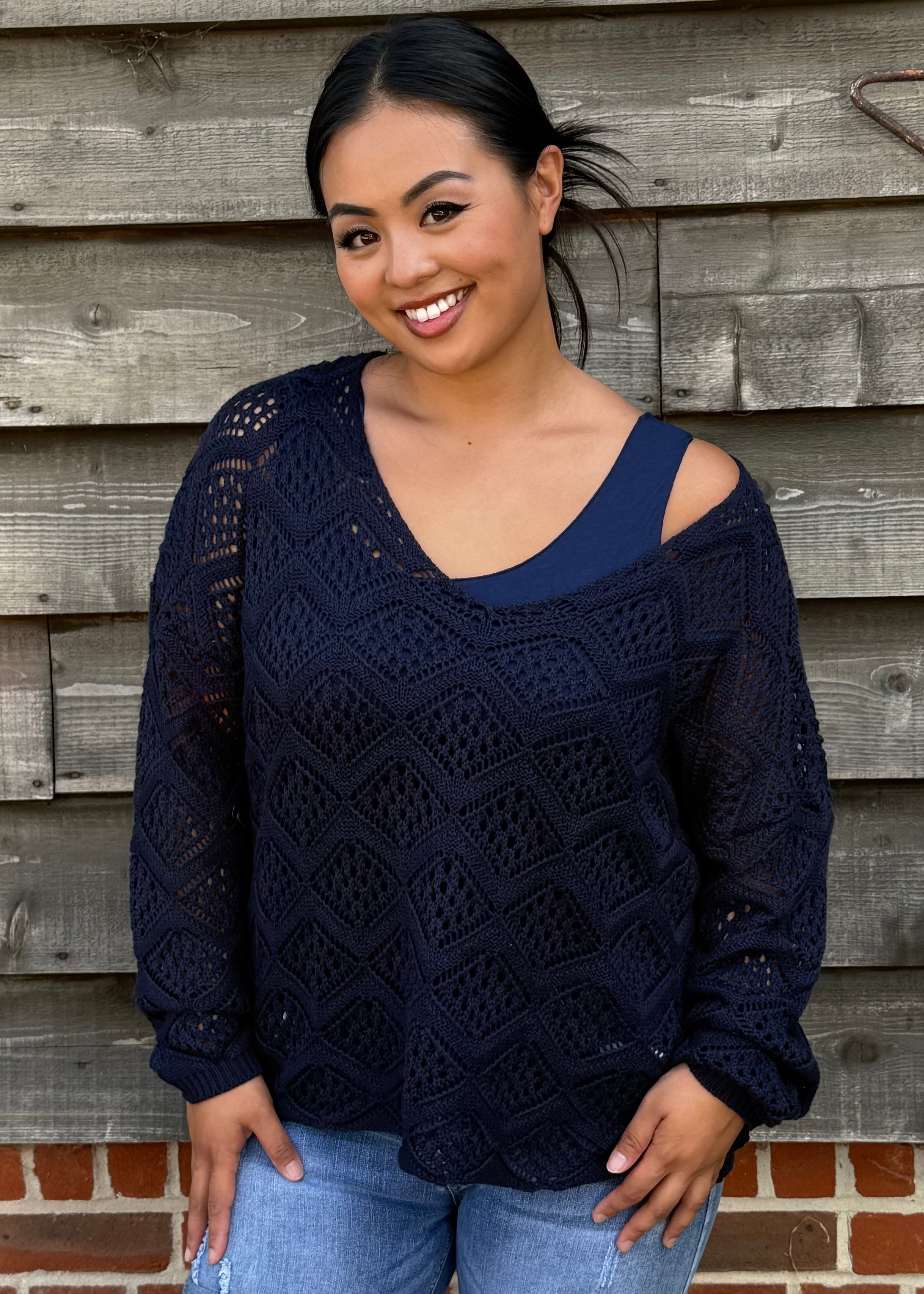 Woman wearing a navy blue sweater with cut-out shoulders against a wooden wall.