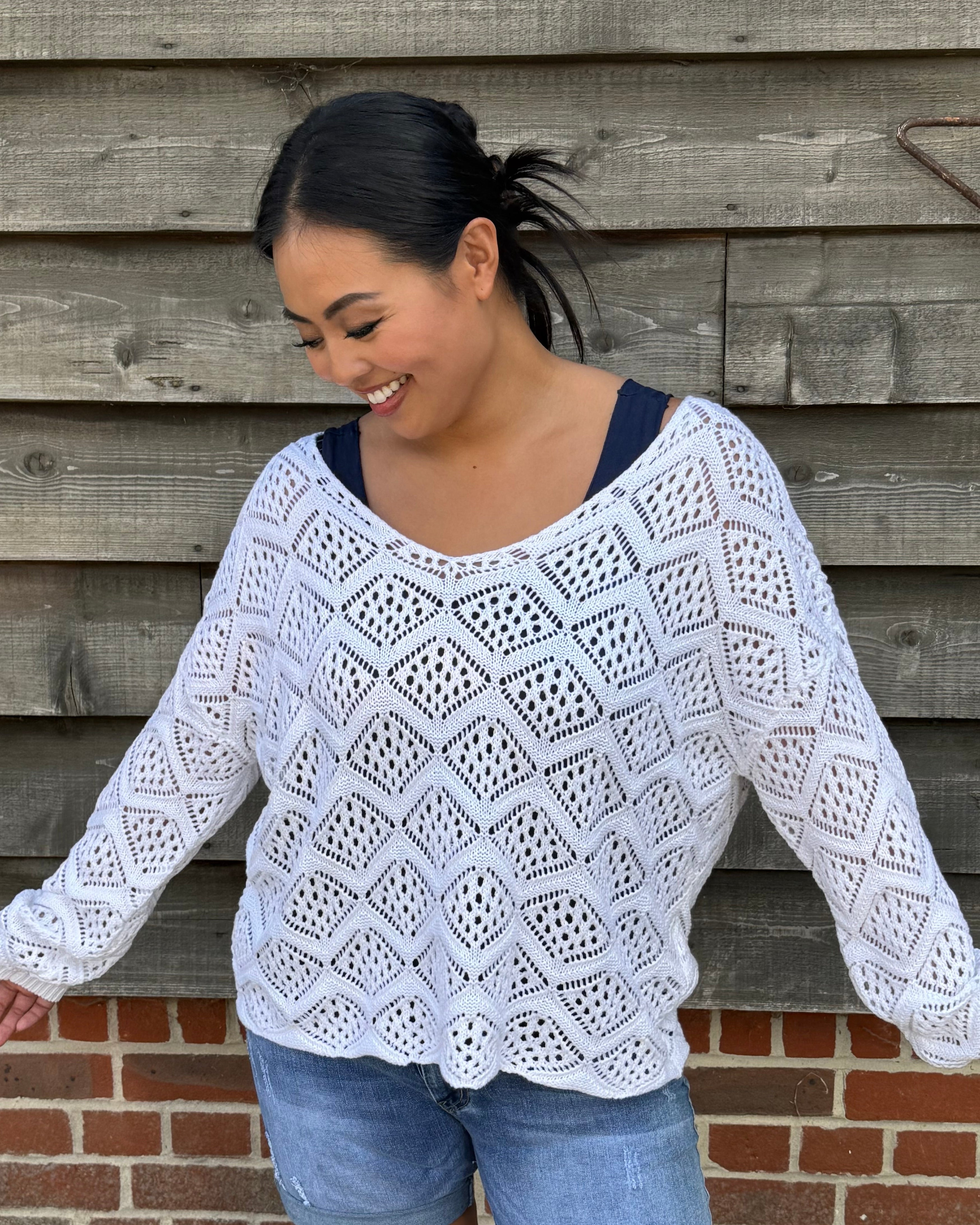 Woman wearing a white crochet top and denim shorts standing against a wooden wall.