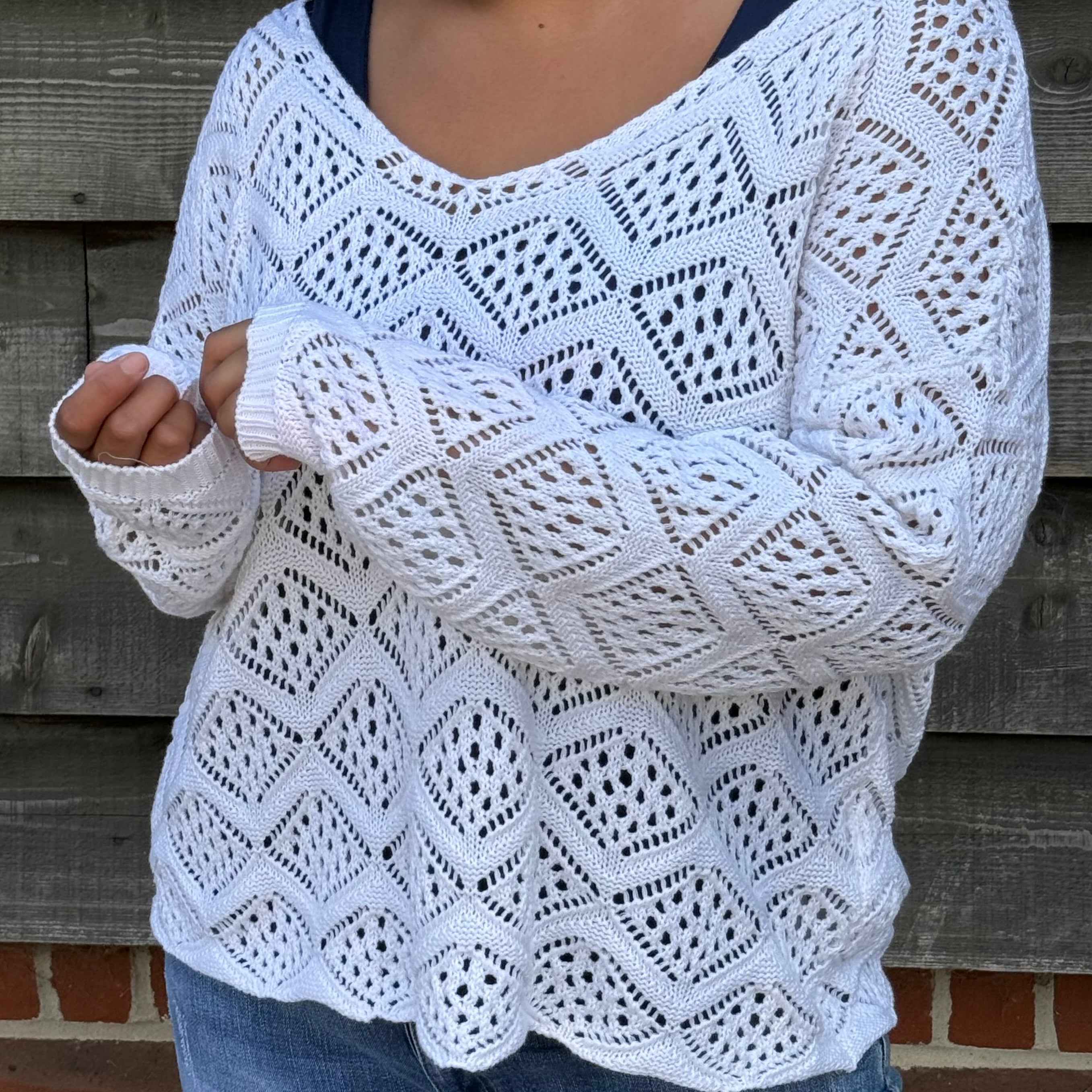 Person wearing a white crochet sweater against a wooden wall.