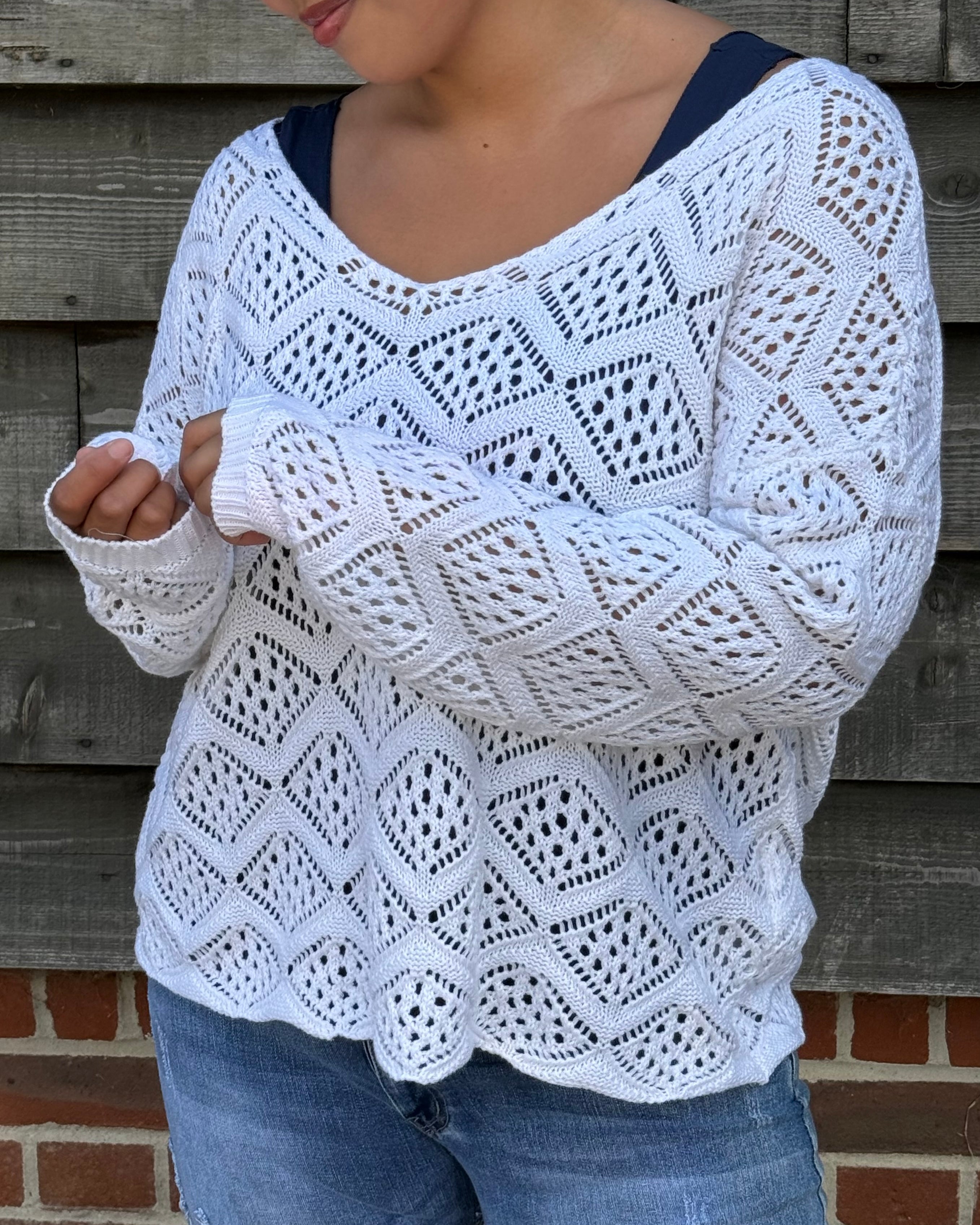 Person wearing a white crochet sweater against a wooden wall.