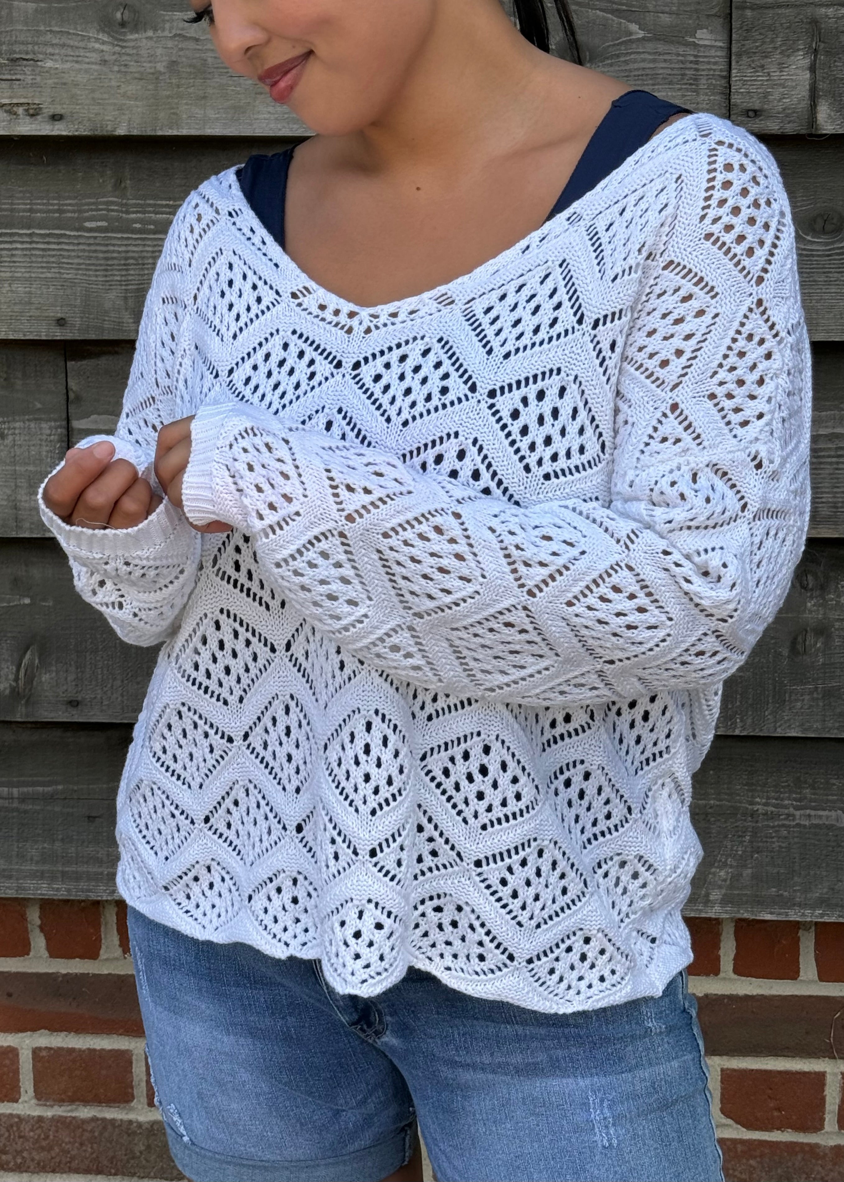 Person wearing a white crochet sweater against a wooden wall.