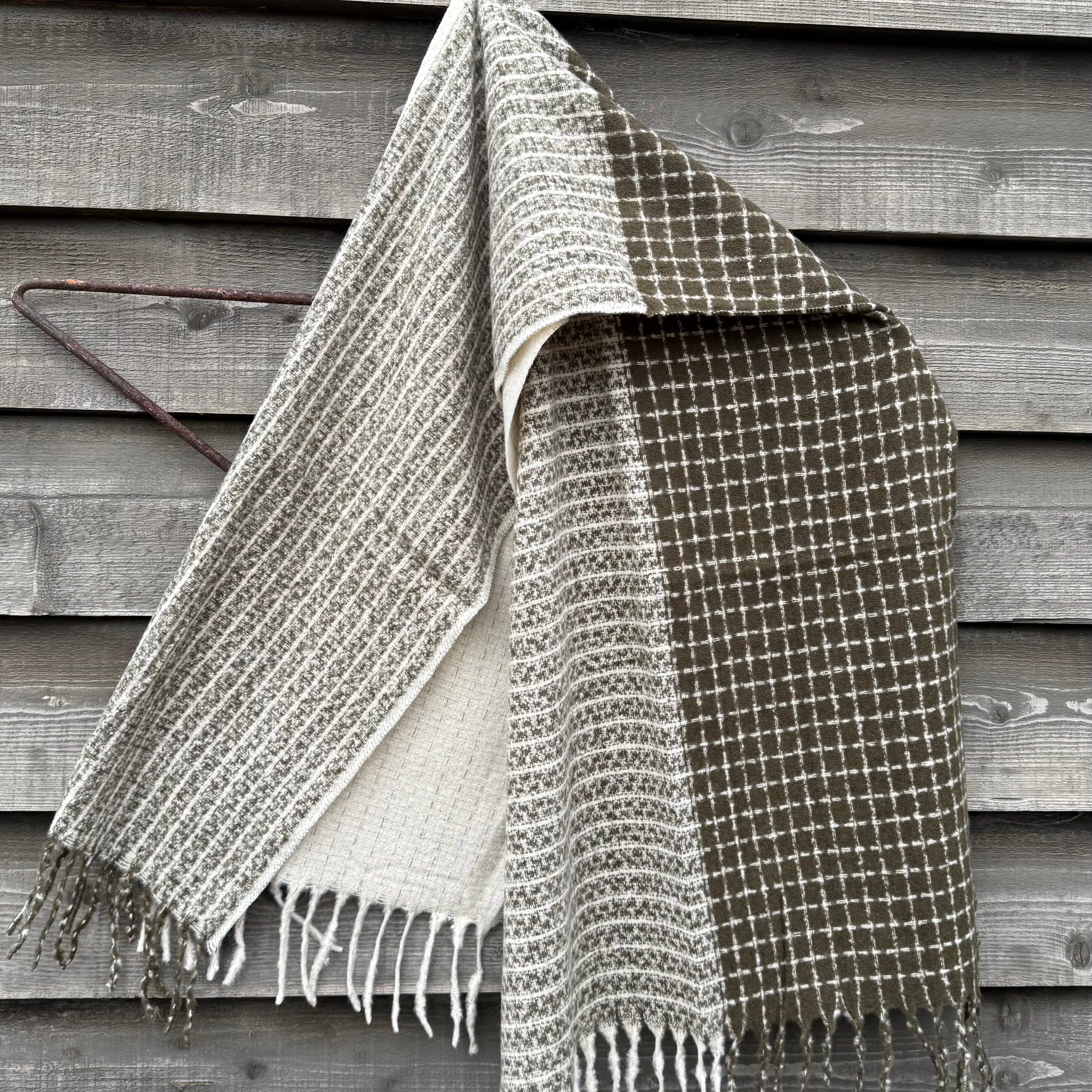 Woven blanket with fringes draped over a wooden surface