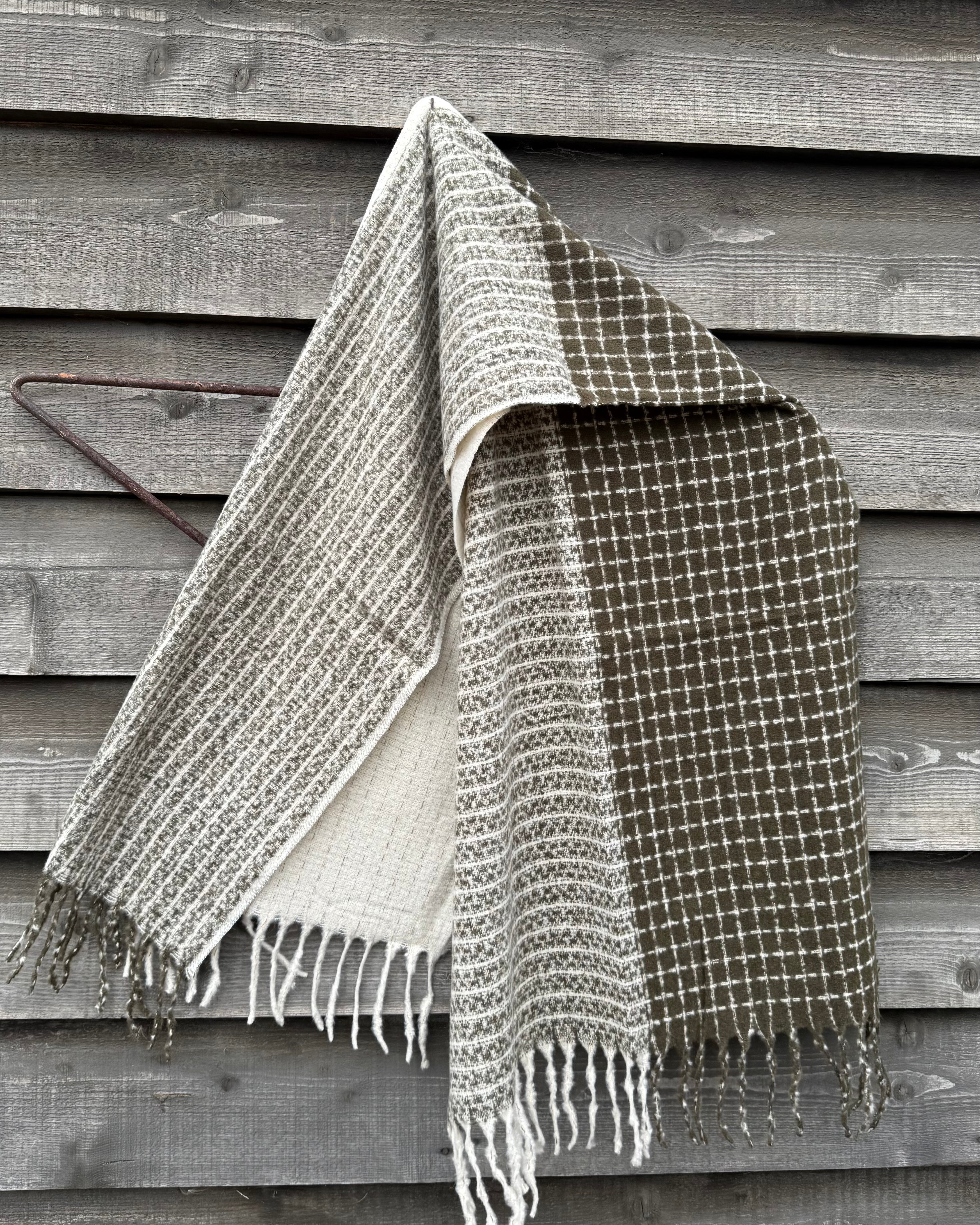 Woven blanket with fringes draped over a wooden surface