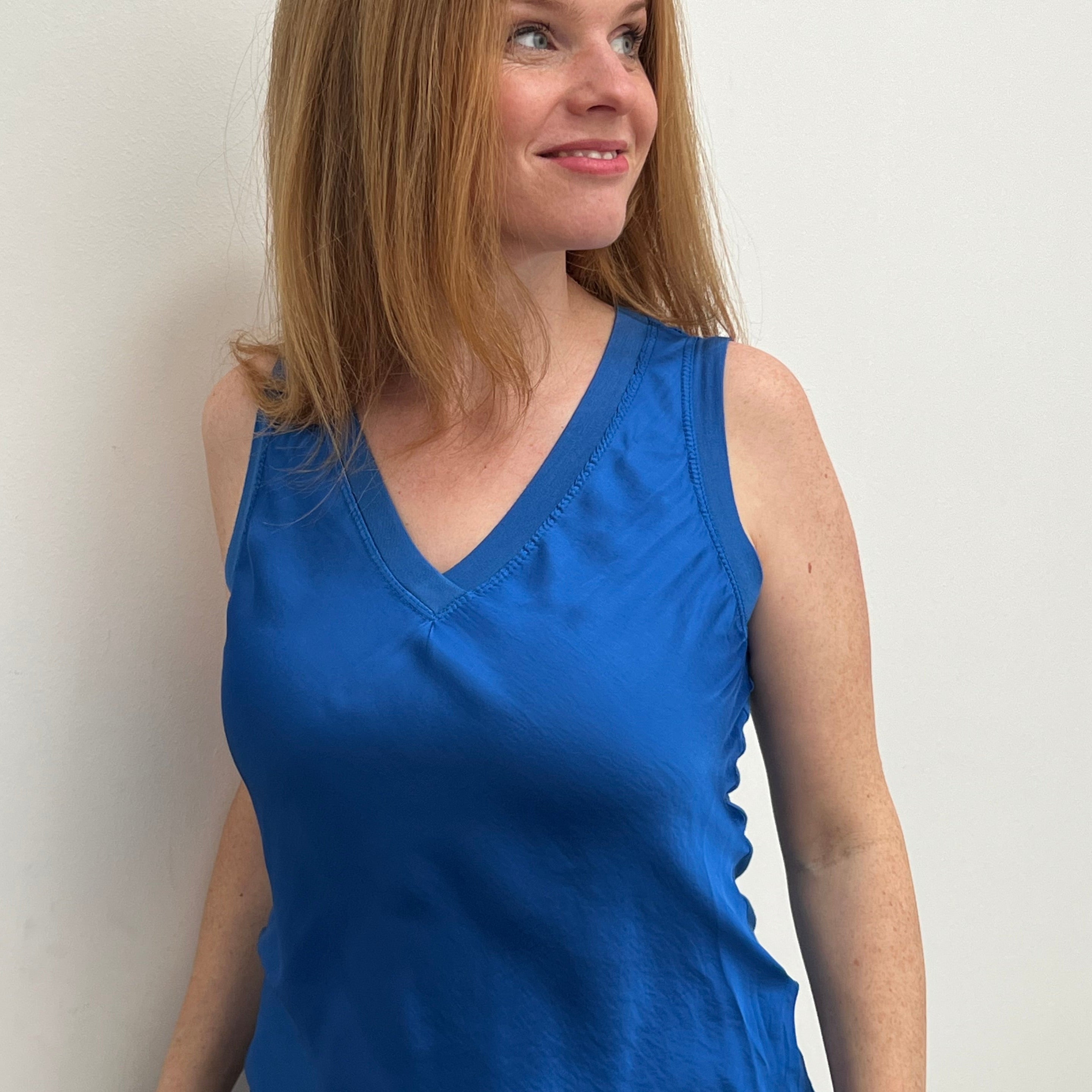 A woman smiling and wearing a blue sleeveless top with a V-neckline, made of silk and viscose fabric.