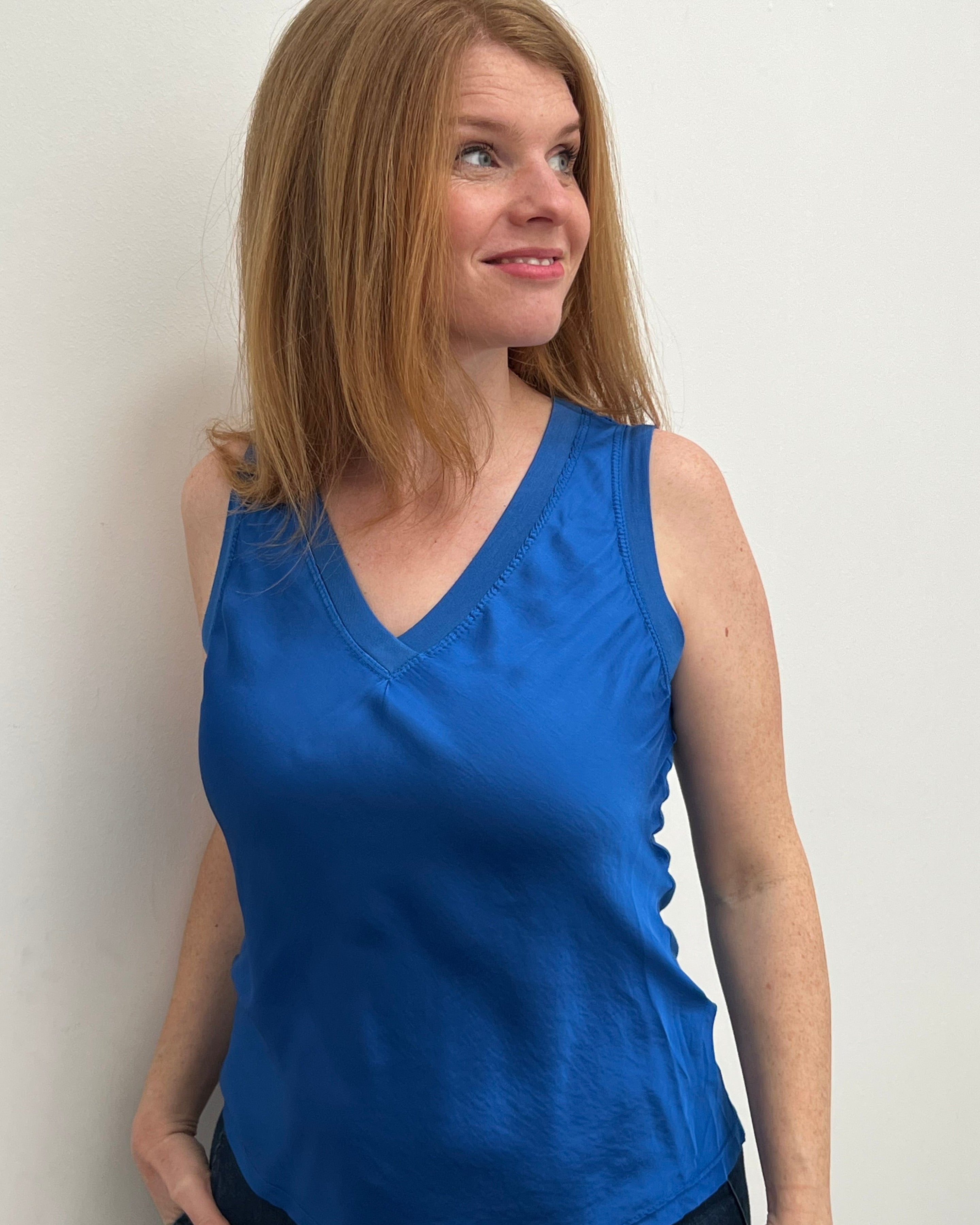 A woman smiling and wearing a blue sleeveless top with a V-neckline, made of silk and viscose fabric.