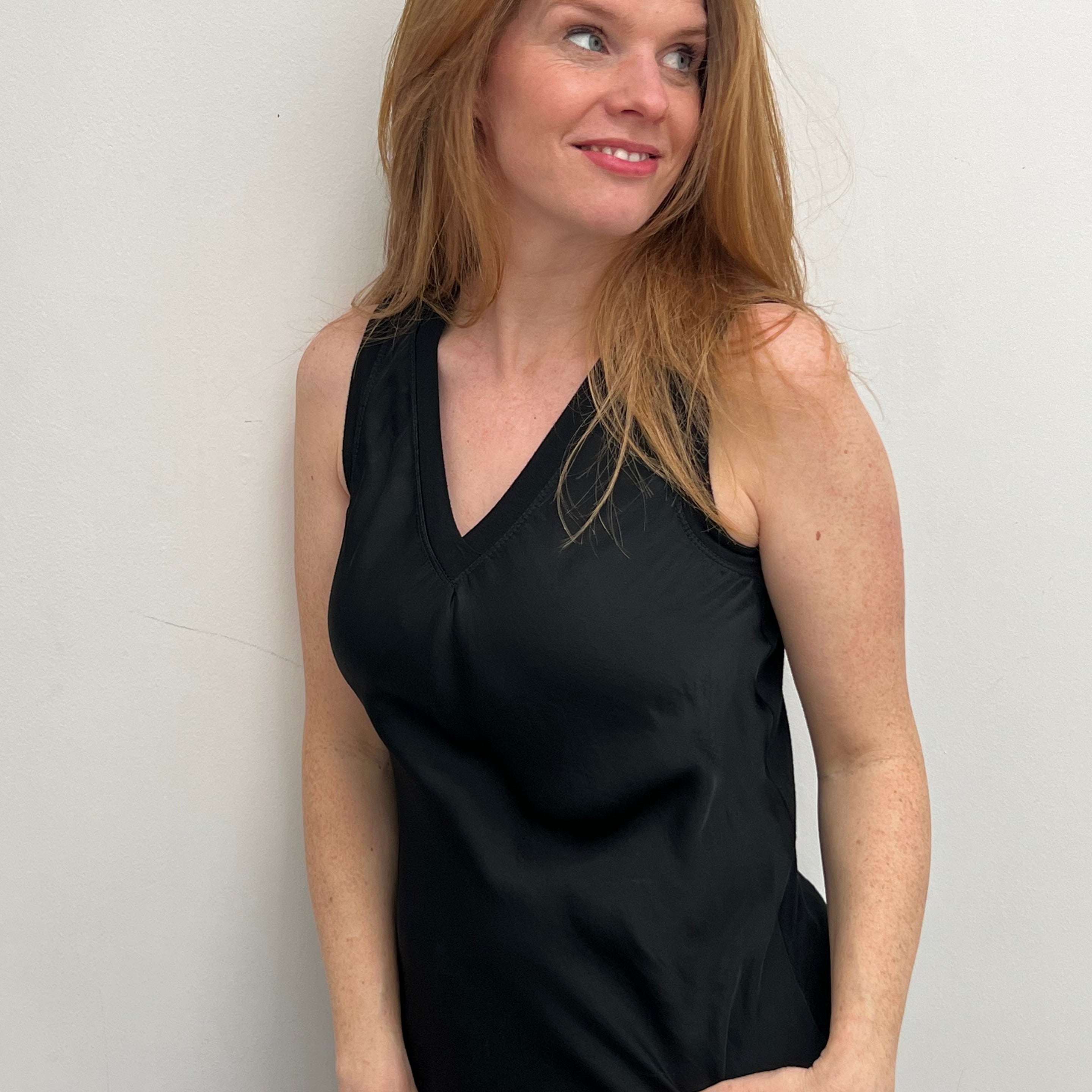 A woman smiling and wearing a black sleeveless top with a V-neckline, made of silk and viscose fabric.