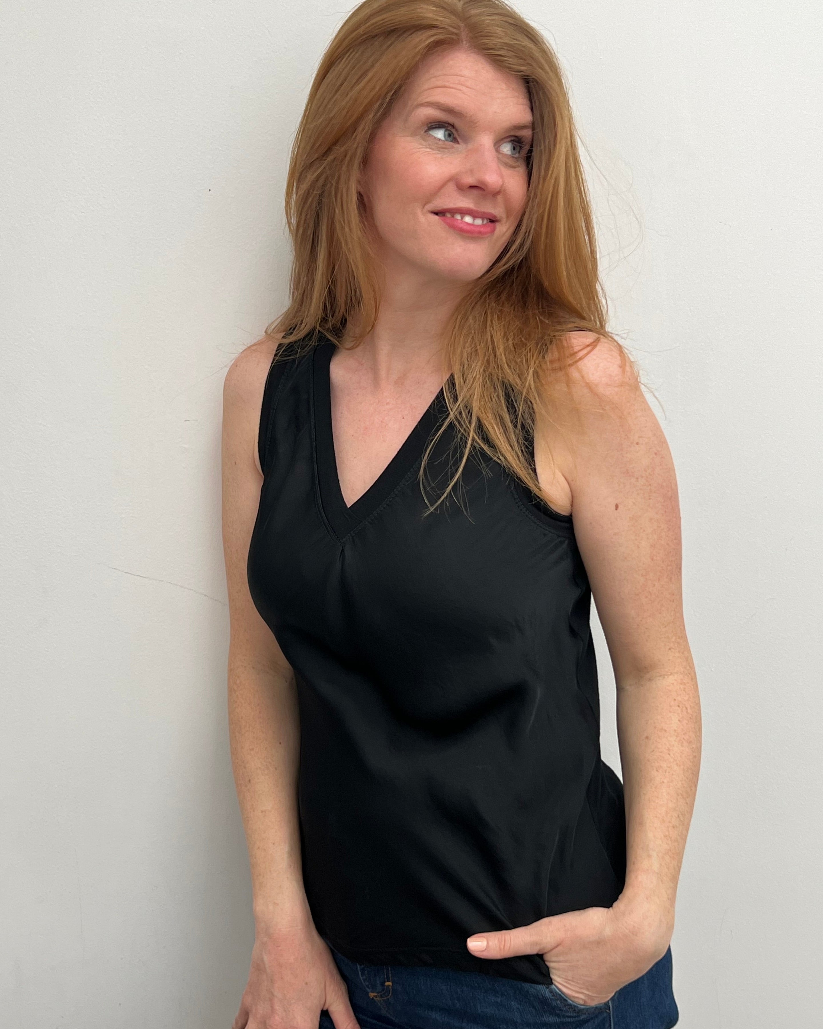 A woman smiling and wearing a black sleeveless top with a V-neckline, made of silk and viscose fabric.