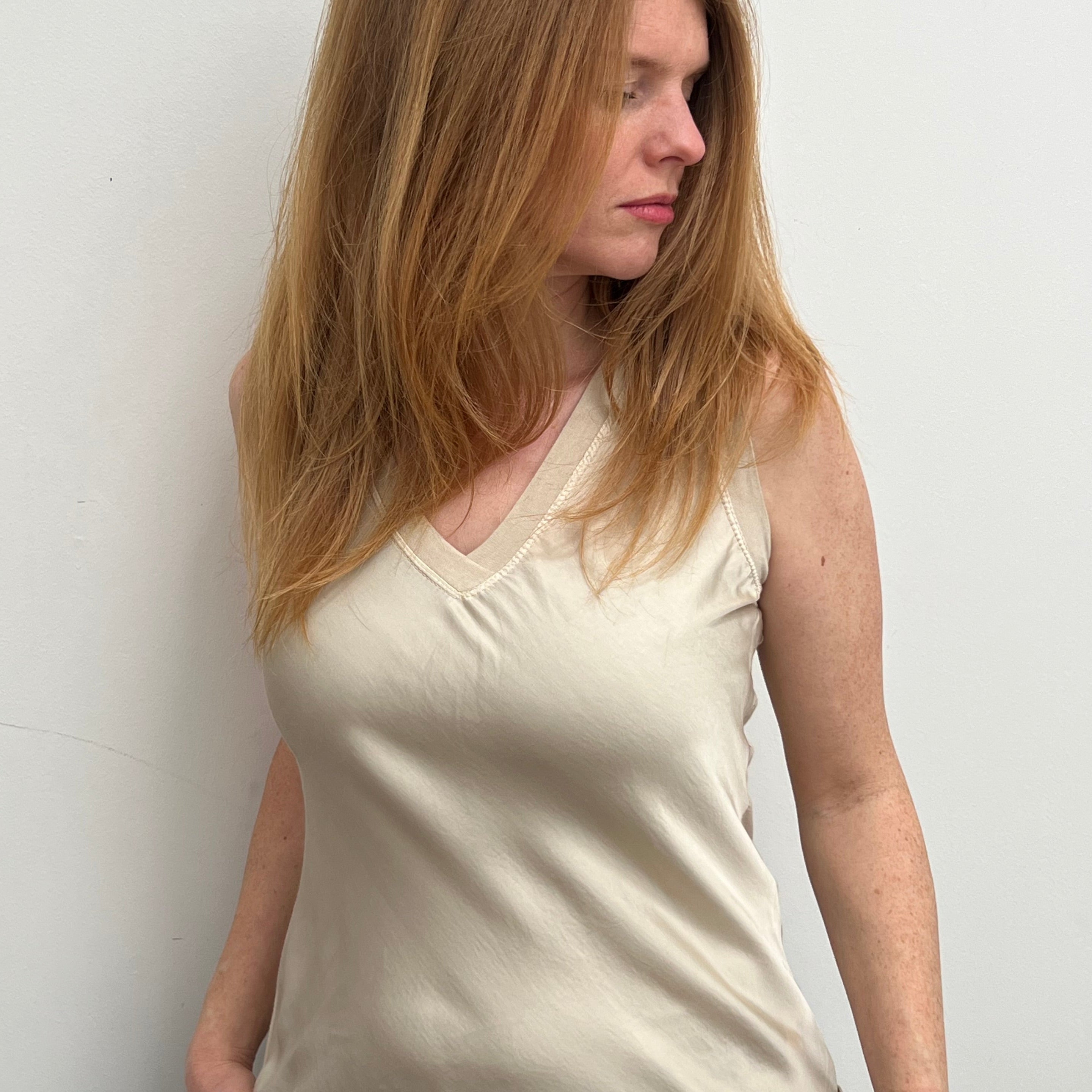 A woman smiling and wearing a beige sleeveless top with a V-neckline, made of silk and viscose fabric.