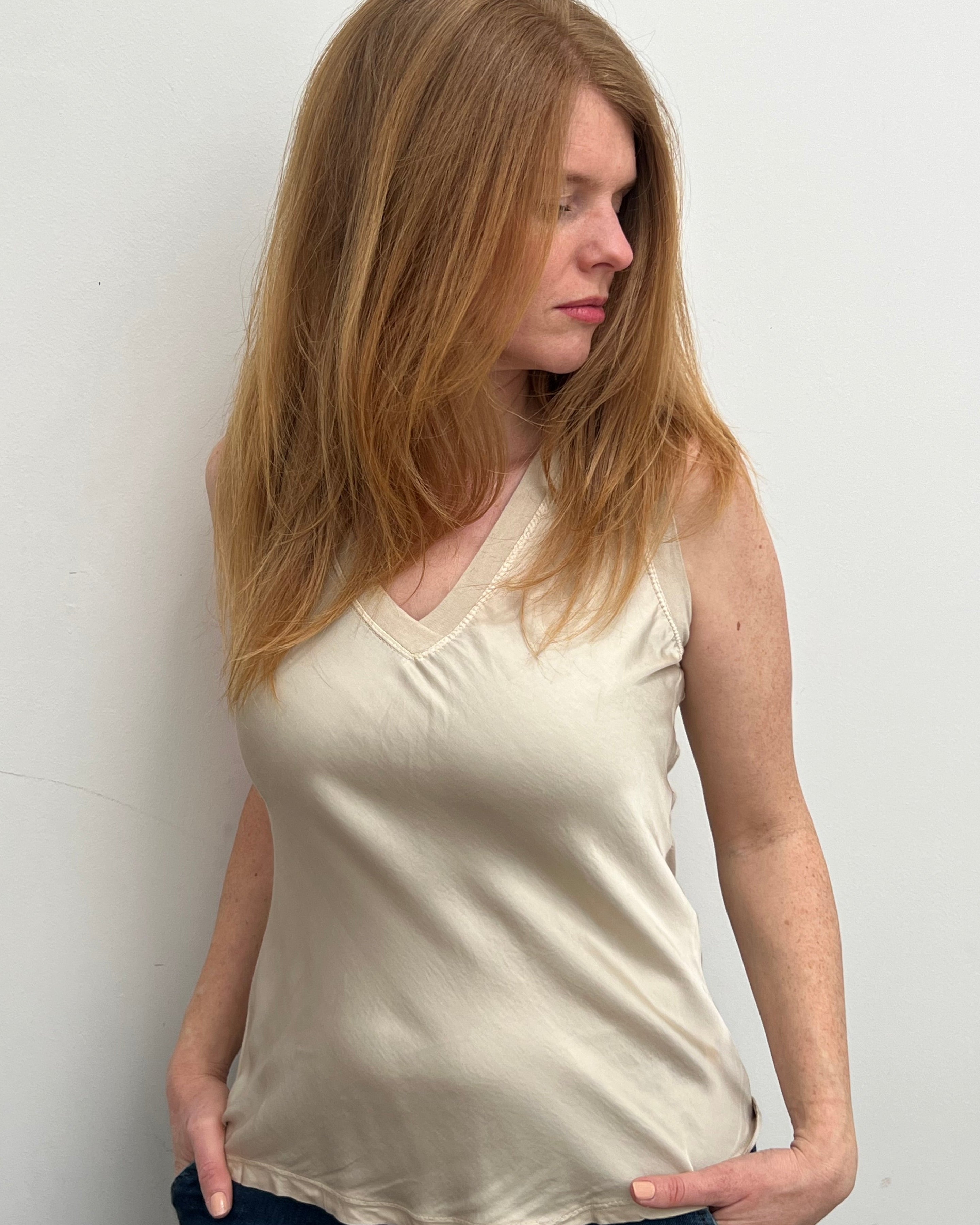 A woman smiling and wearing a beige sleeveless top with a V-neckline, made of silk and viscose fabric.