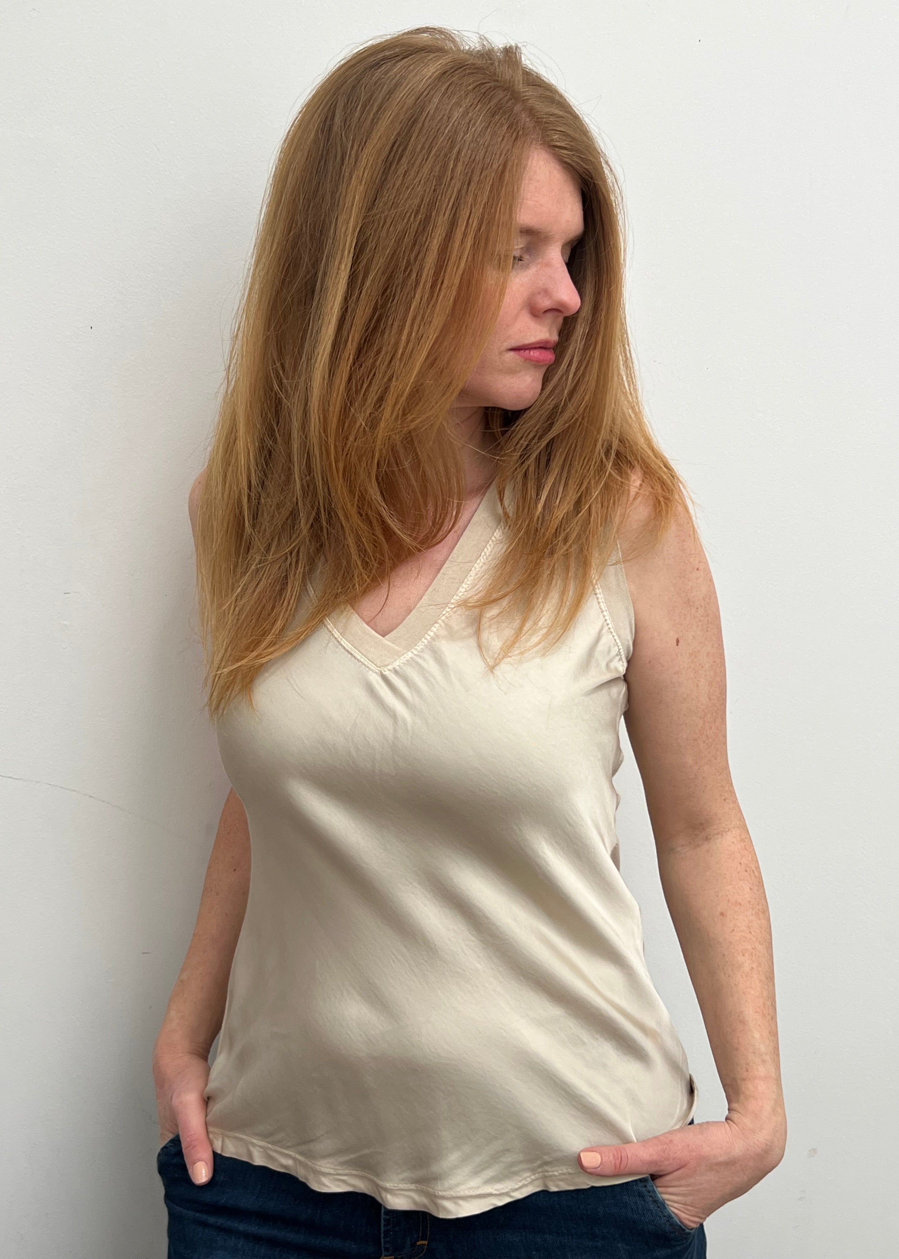 A woman smiling and wearing a beige sleeveless top with a V-neckline, made of silk and viscose fabric.