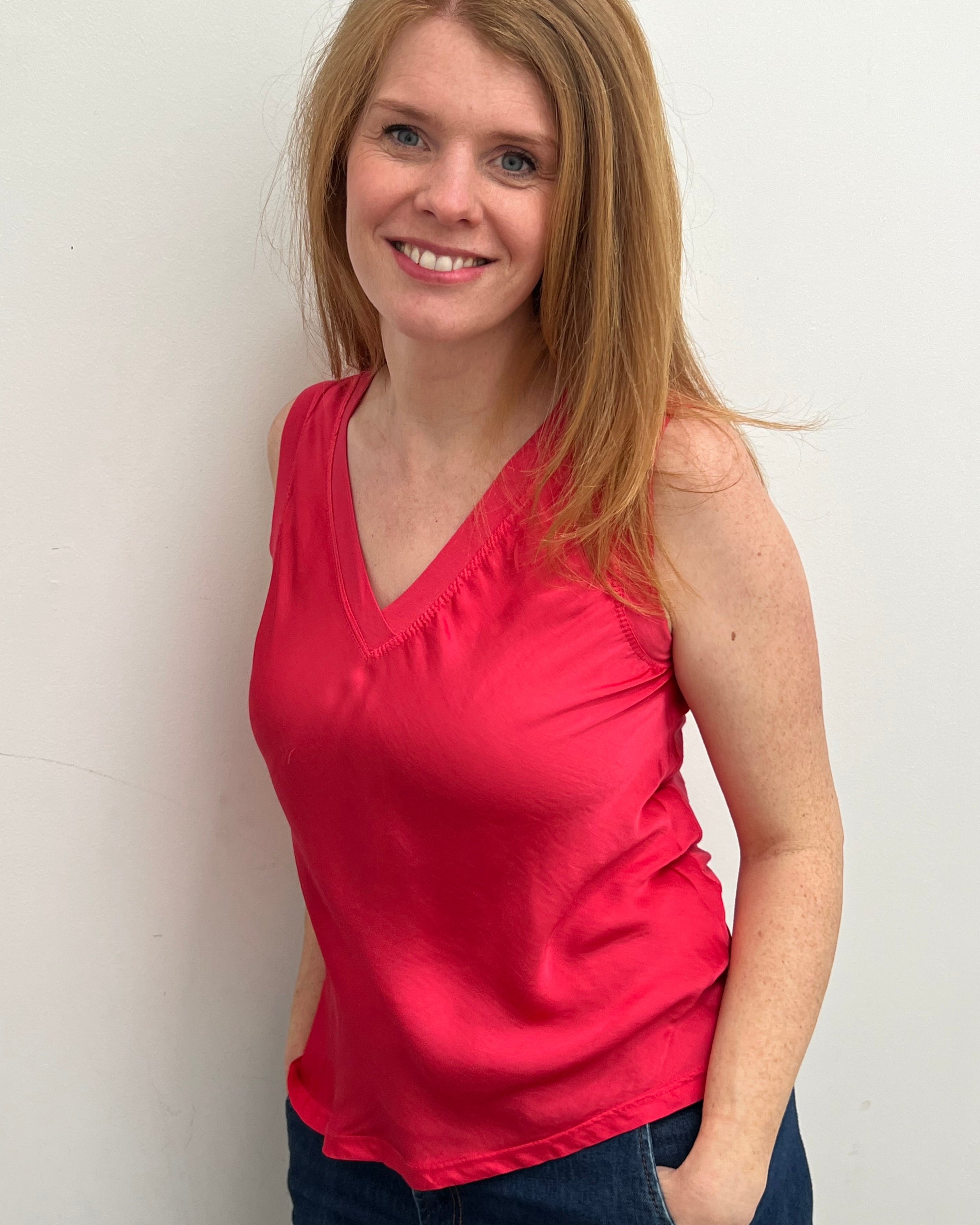 A woman smiling and wearing a red sleeveless top with a V-neckline, made of silk and viscose fabric.