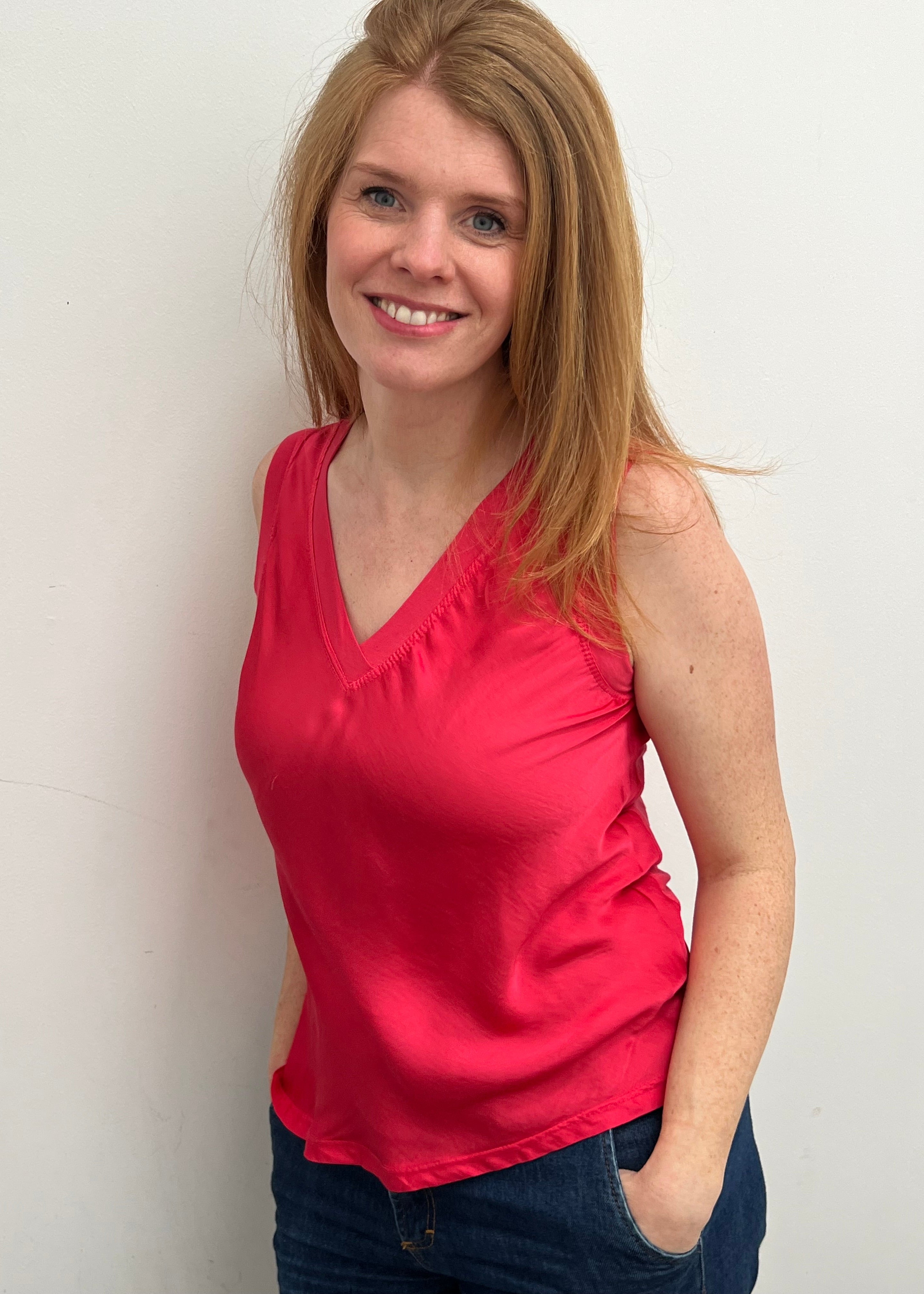 A woman smiling and wearing a red sleeveless top with a V-neckline, made of silk and viscose fabric.