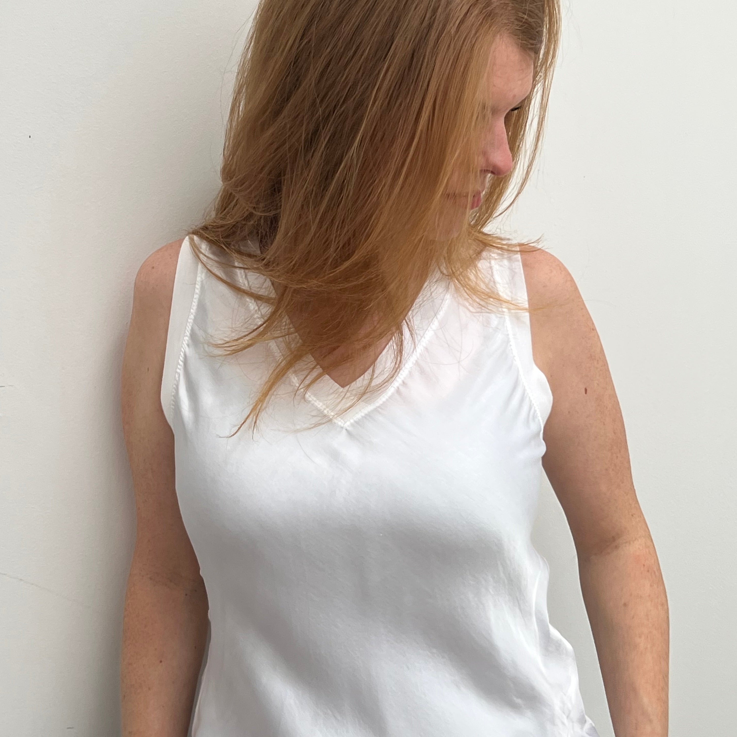 A woman smiling and wearing a blue sleeveless top with a V-neckline, made of silk and viscose fabric.