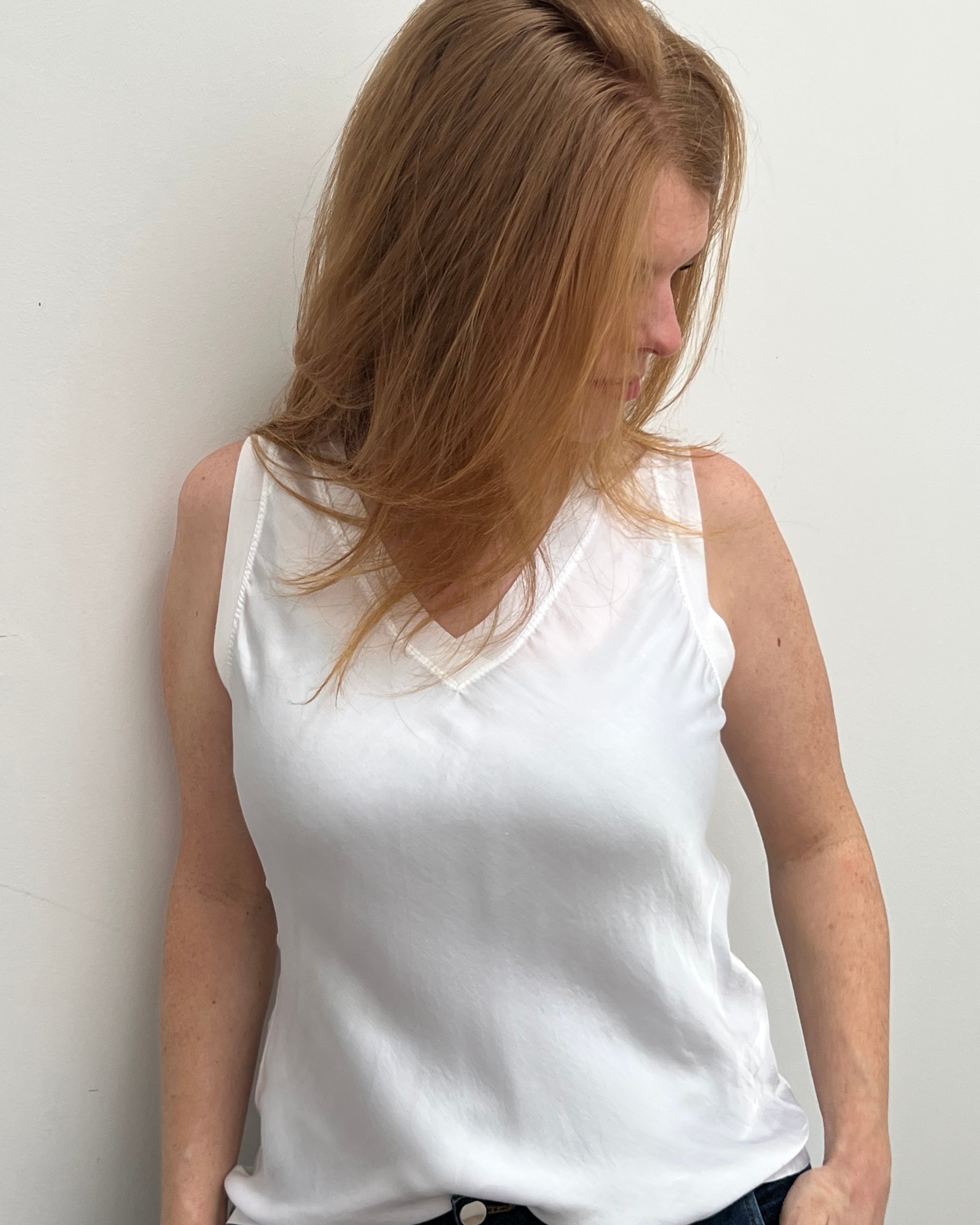 A woman smiling and wearing a blue sleeveless top with a V-neckline, made of silk and viscose fabric.