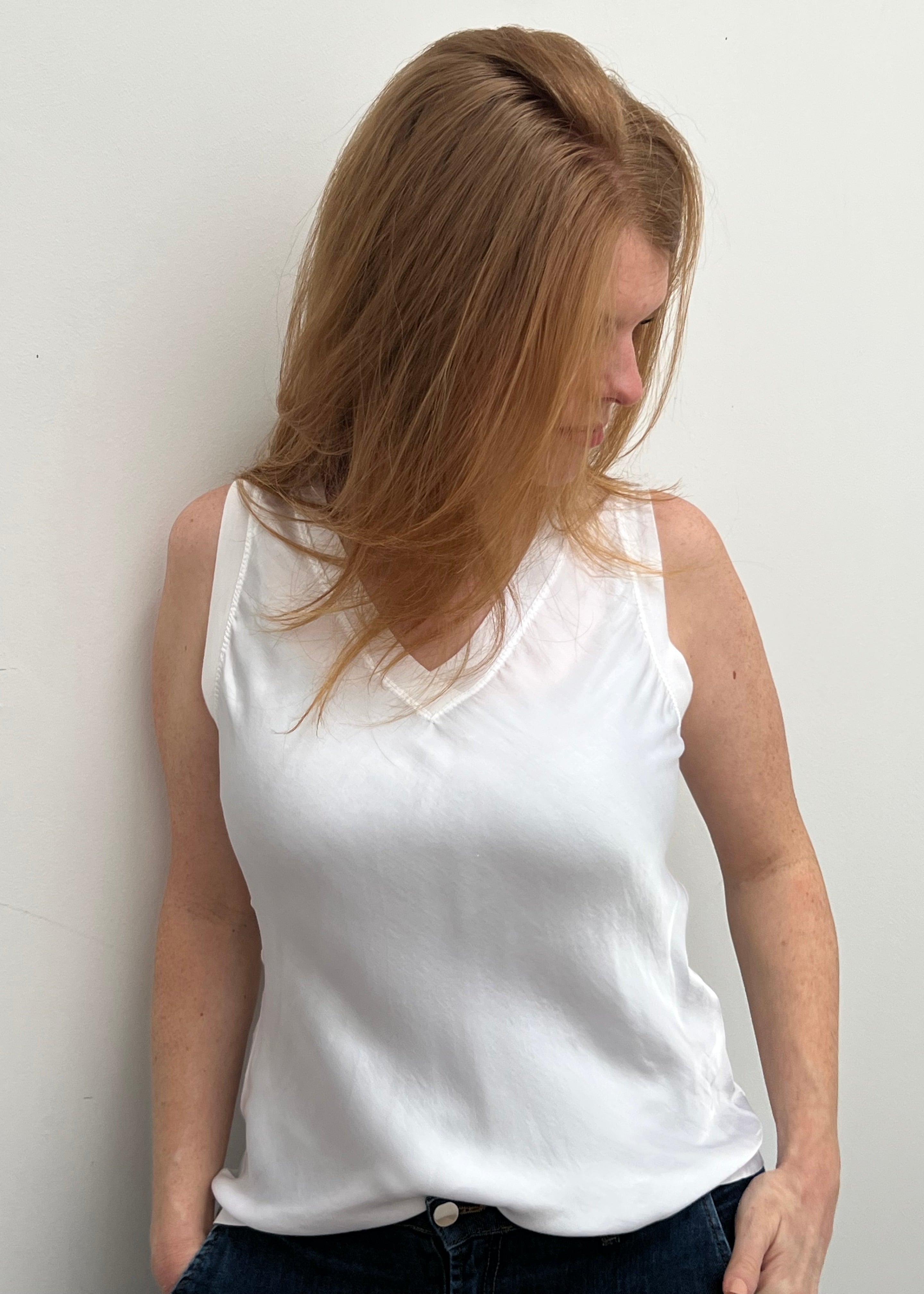 A woman smiling and wearing a blue sleeveless top with a V-neckline, made of silk and viscose fabric.