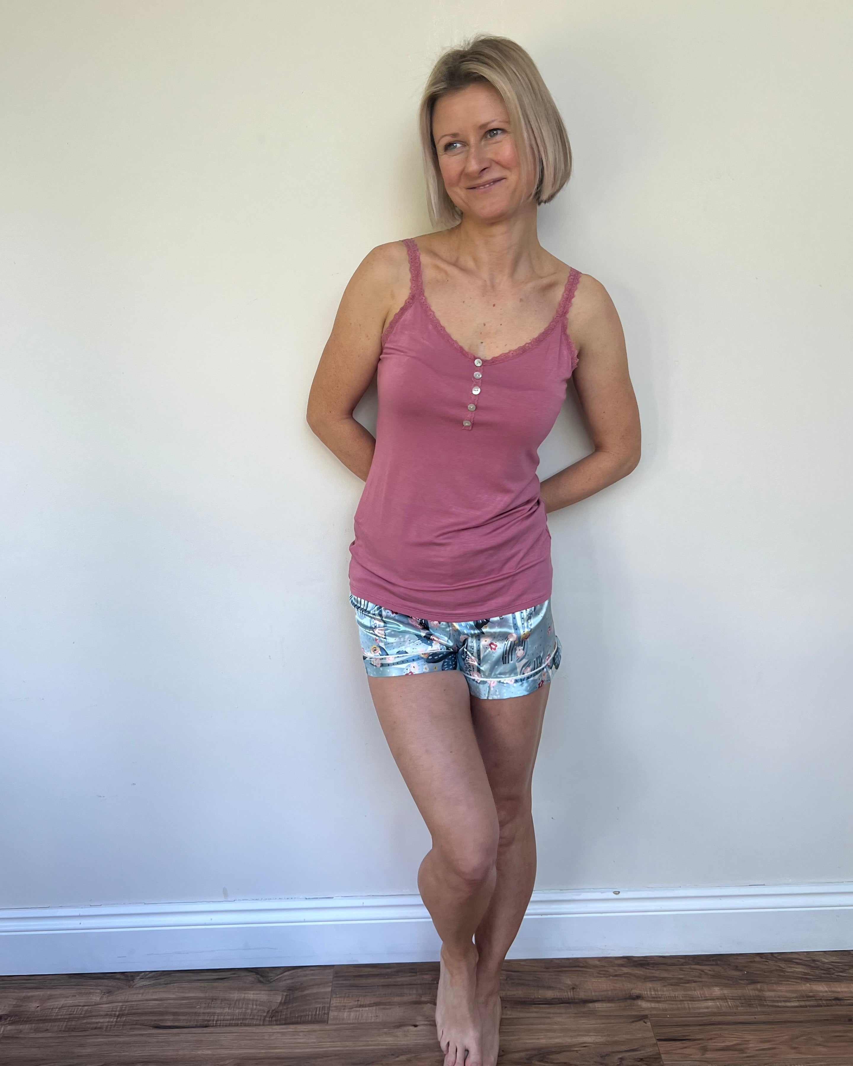 A person wearing a pink tank top and multicolored shorts, standing against a neutral background.