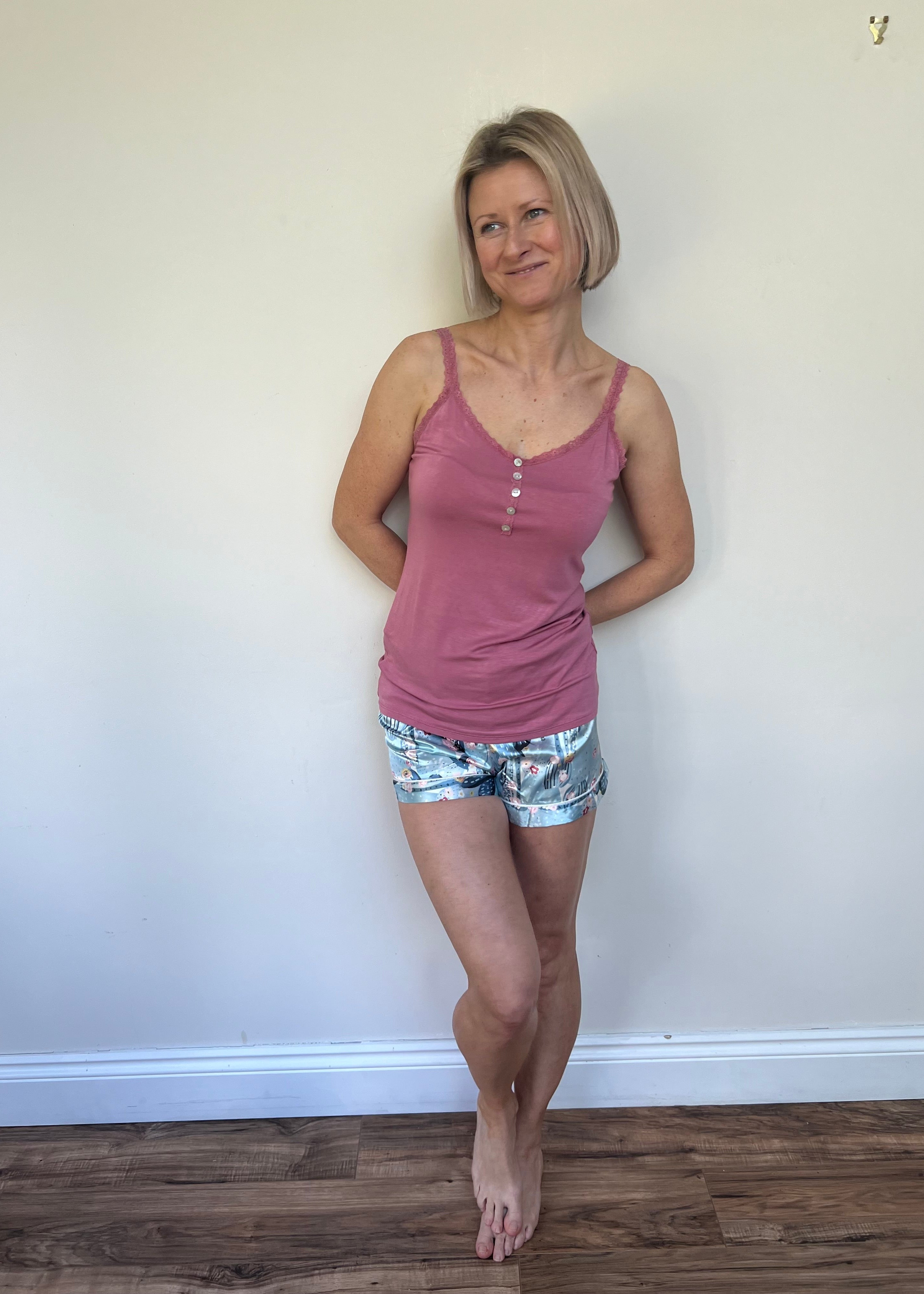 A person wearing a pink tank top and multicolored shorts, standing against a neutral background.