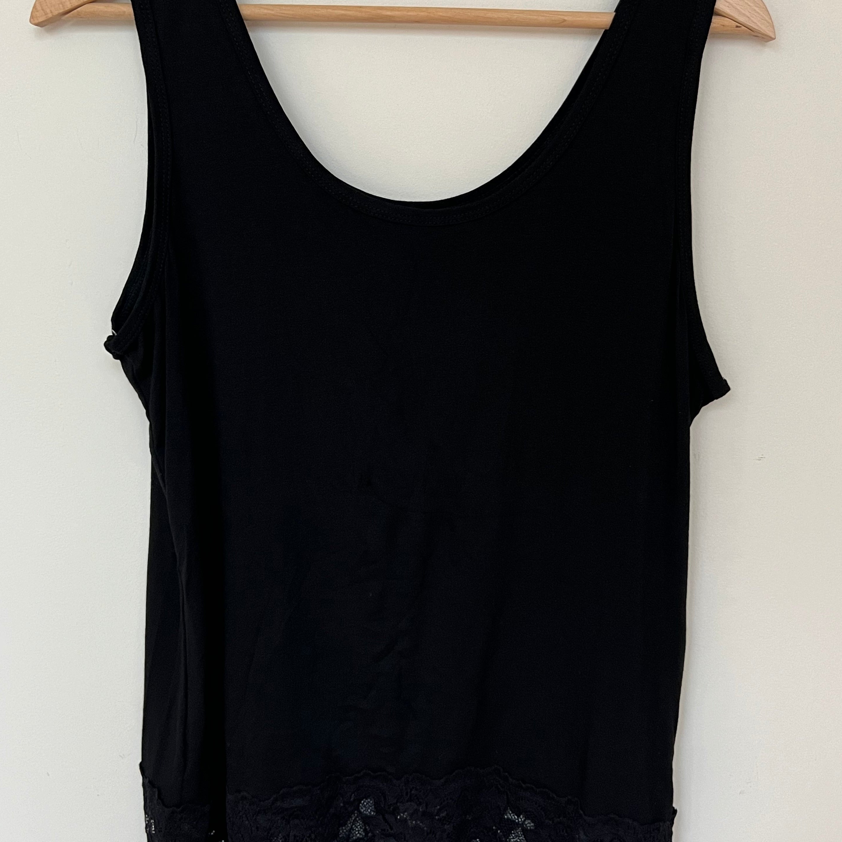 A woman wearing a pink sleeveless vest with a lace hem, paired with blue jeans.