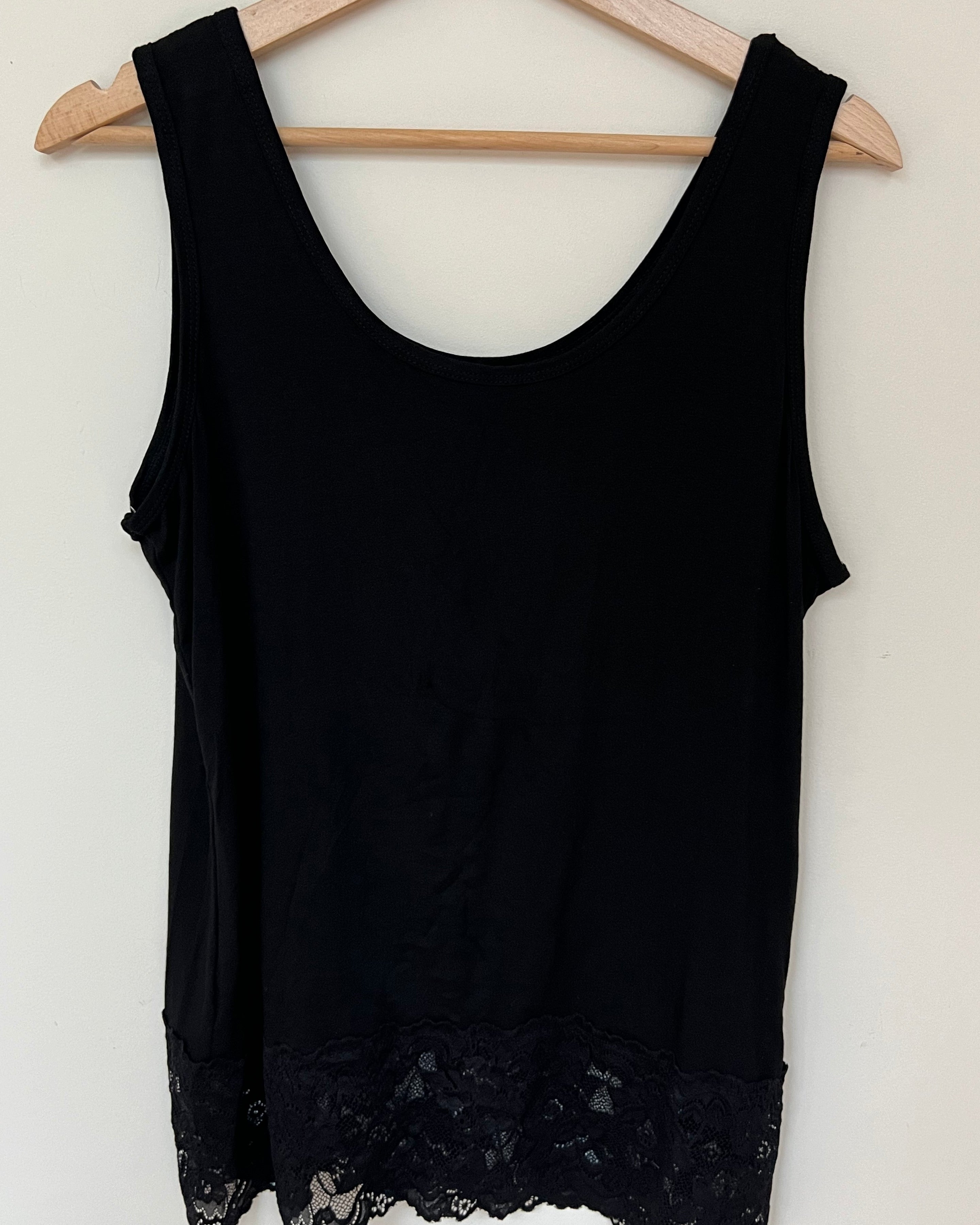 A woman wearing a pink sleeveless vest with a lace hem, paired with blue jeans.