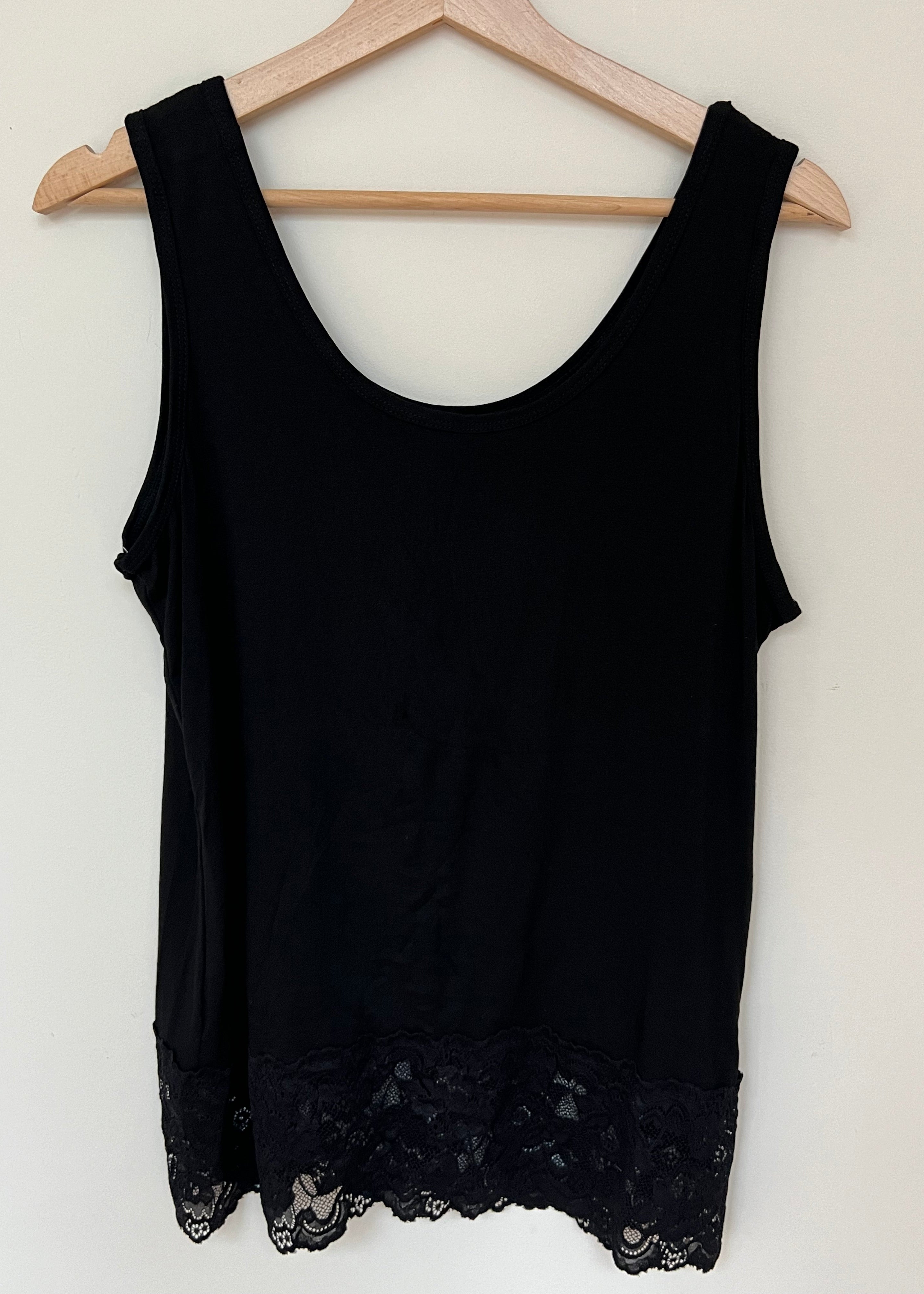 A woman wearing a pink sleeveless vest with a lace hem, paired with blue jeans.