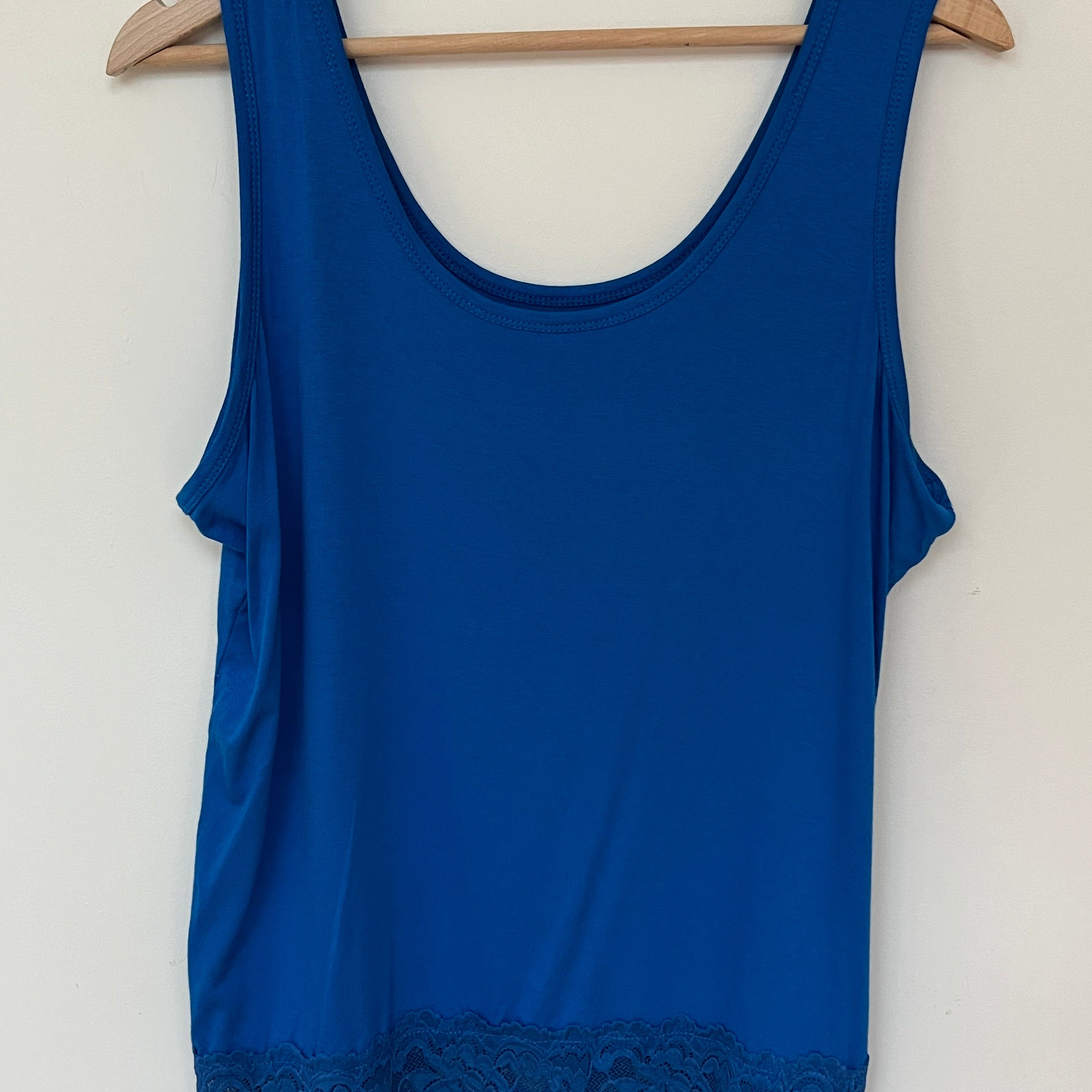 A woman wearing a pink sleeveless vest with a lace hem, paired with blue jeans.