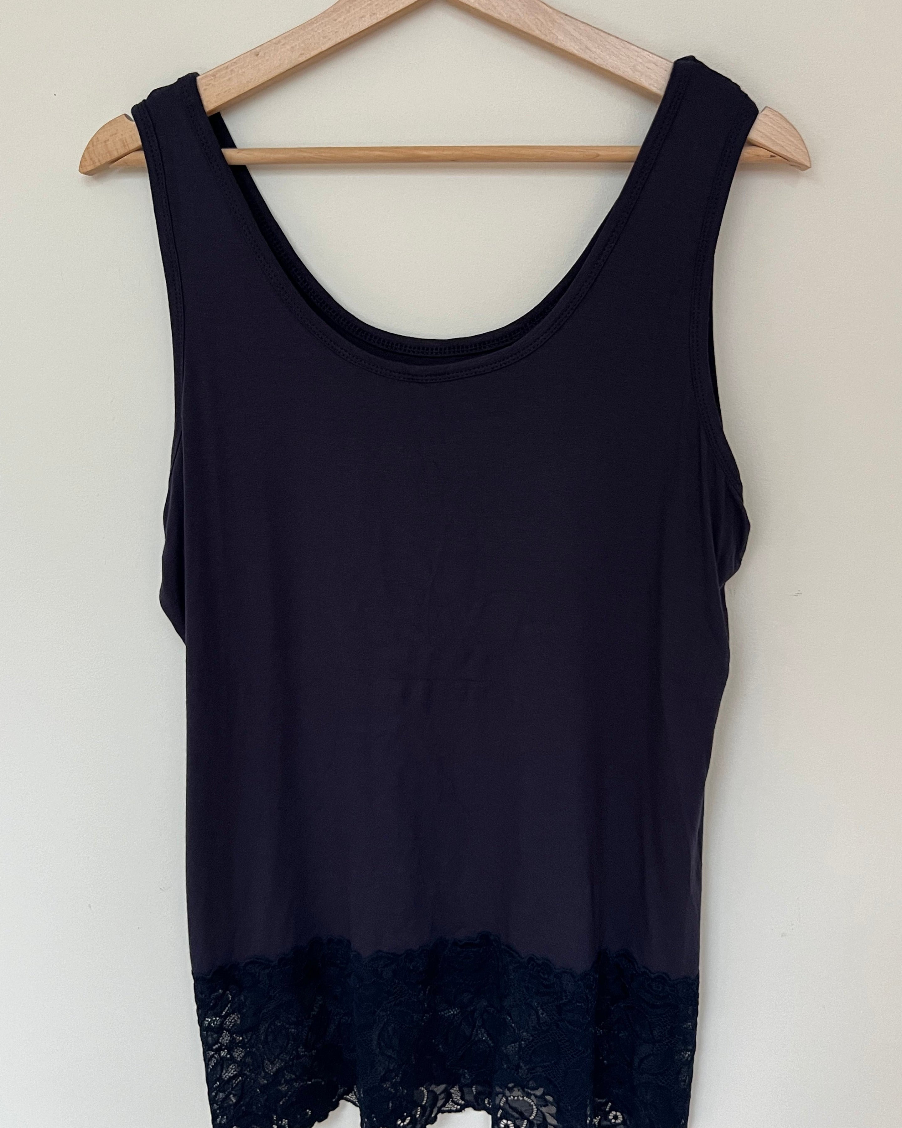 A woman wearing a pink sleeveless vest with a lace hem, paired with blue jeans.