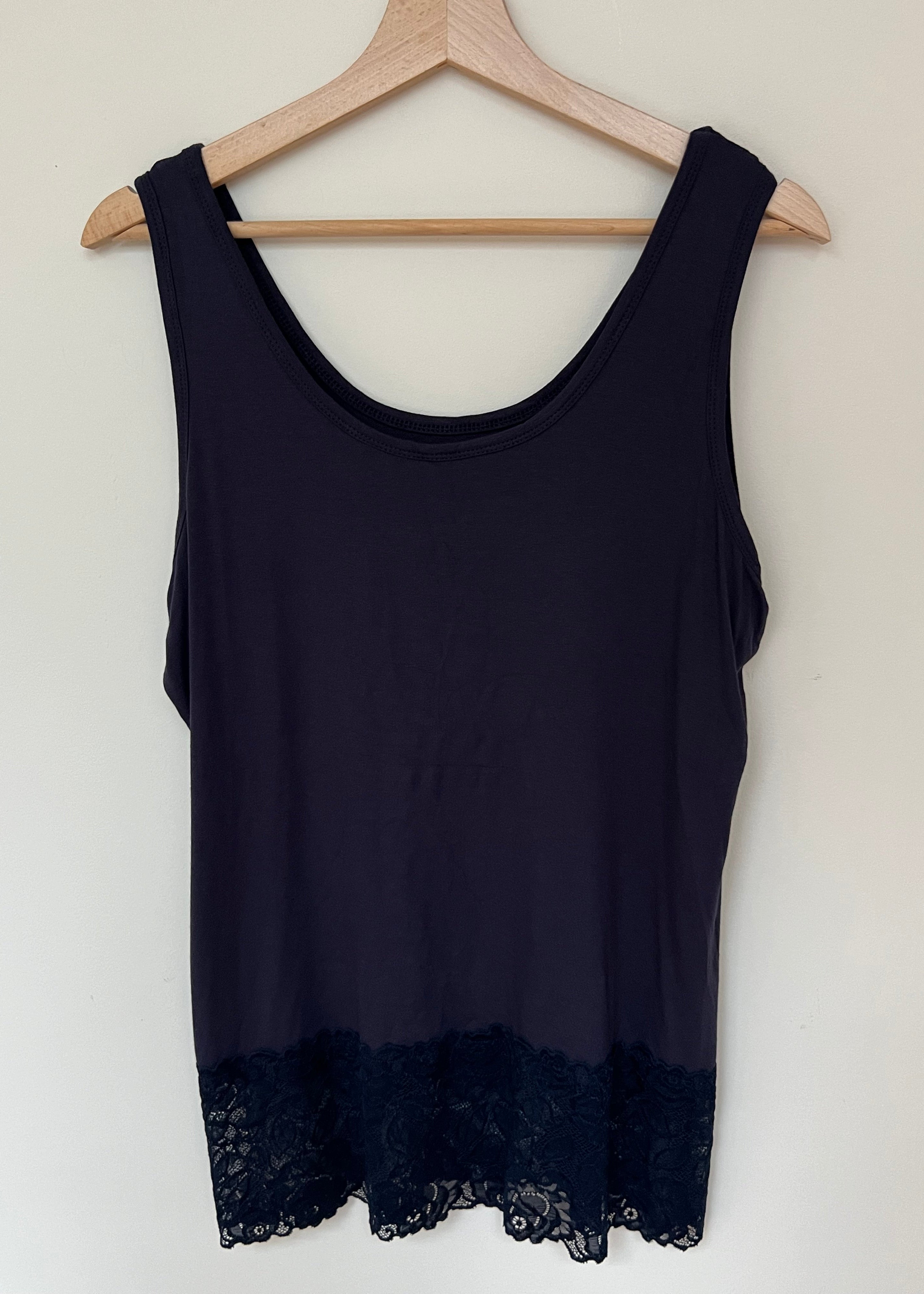 A woman wearing a pink sleeveless vest with a lace hem, paired with blue jeans.