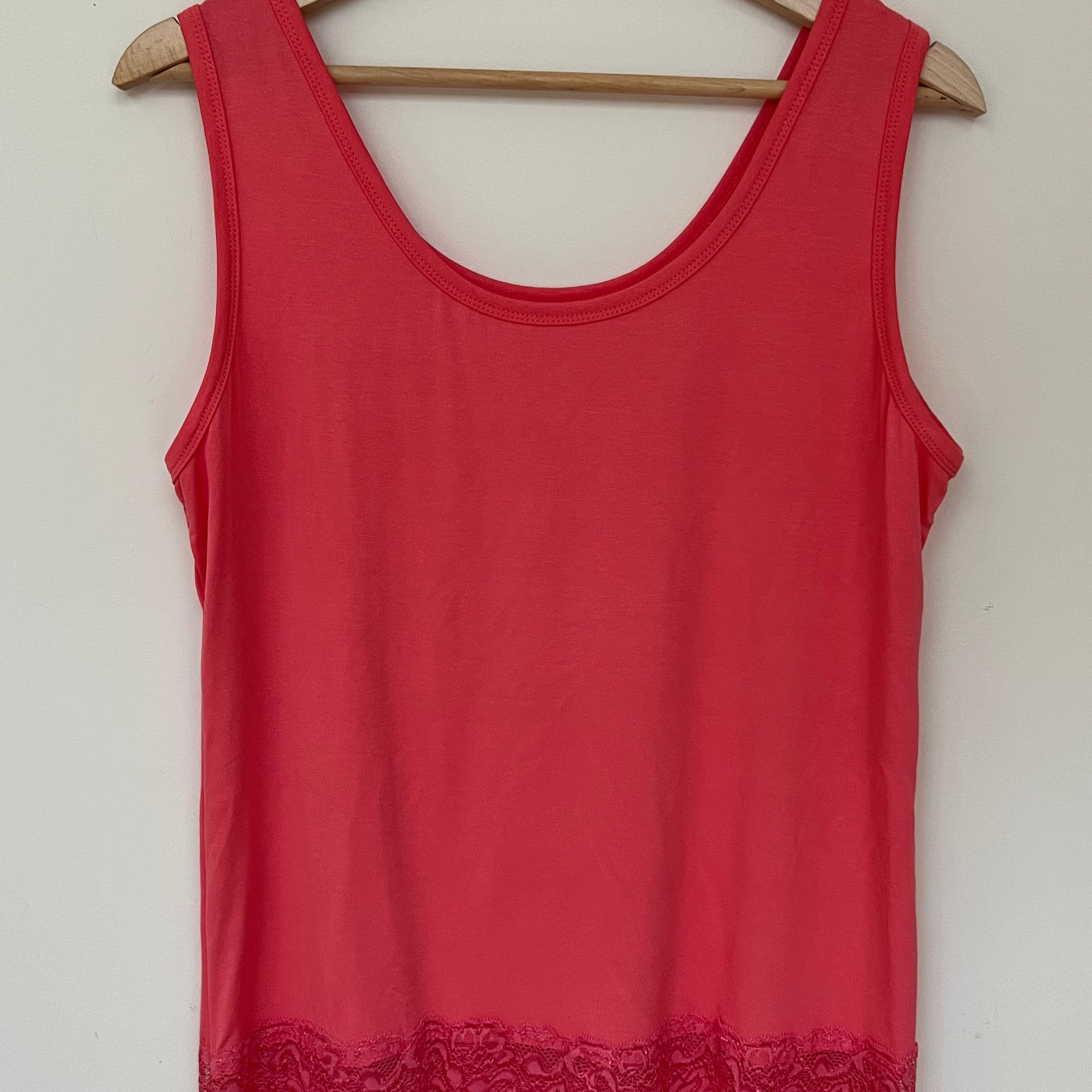 A woman wearing a pink sleeveless vest with a lace hem, paired with blue jeans.