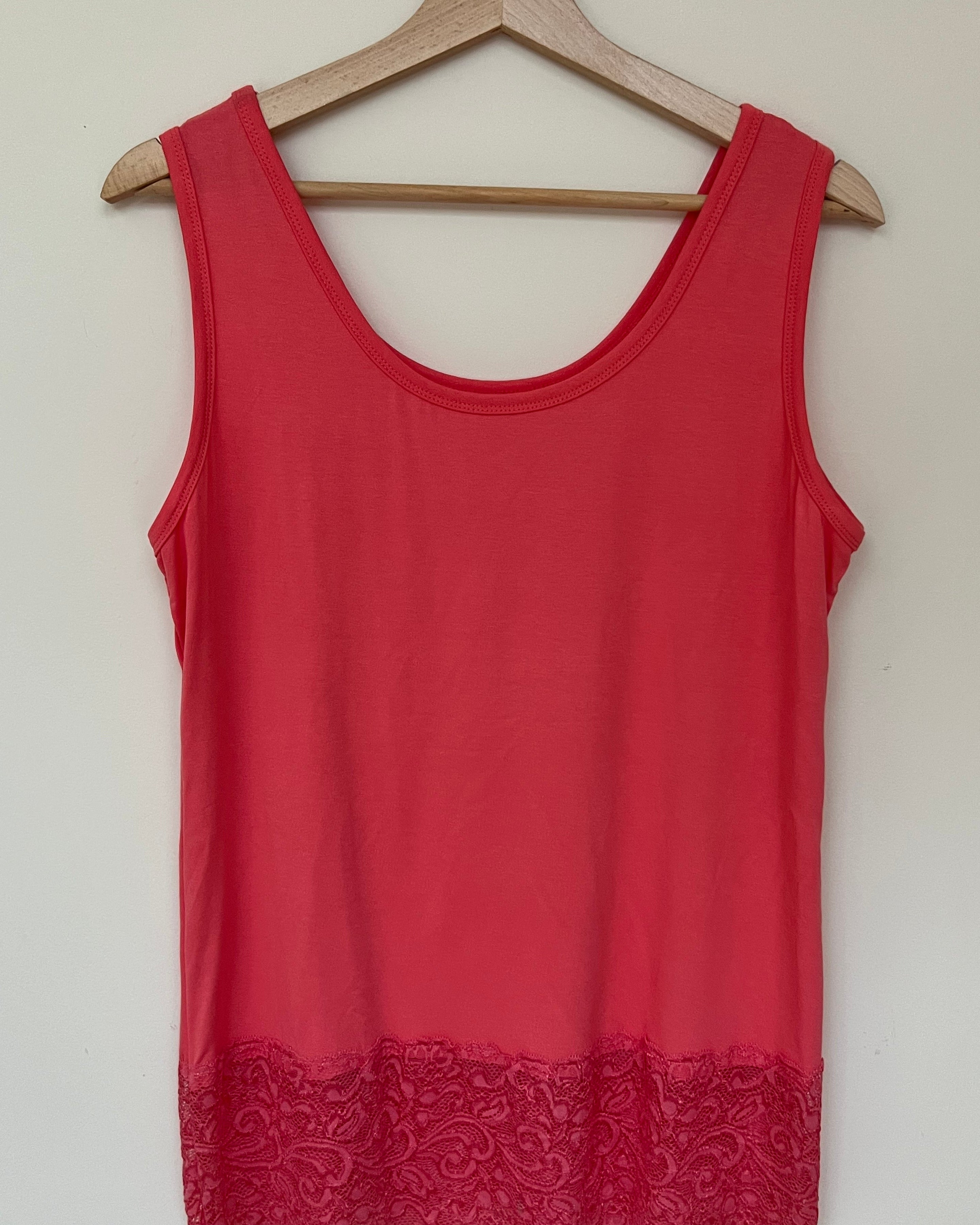 A woman wearing a pink sleeveless vest with a lace hem, paired with blue jeans.