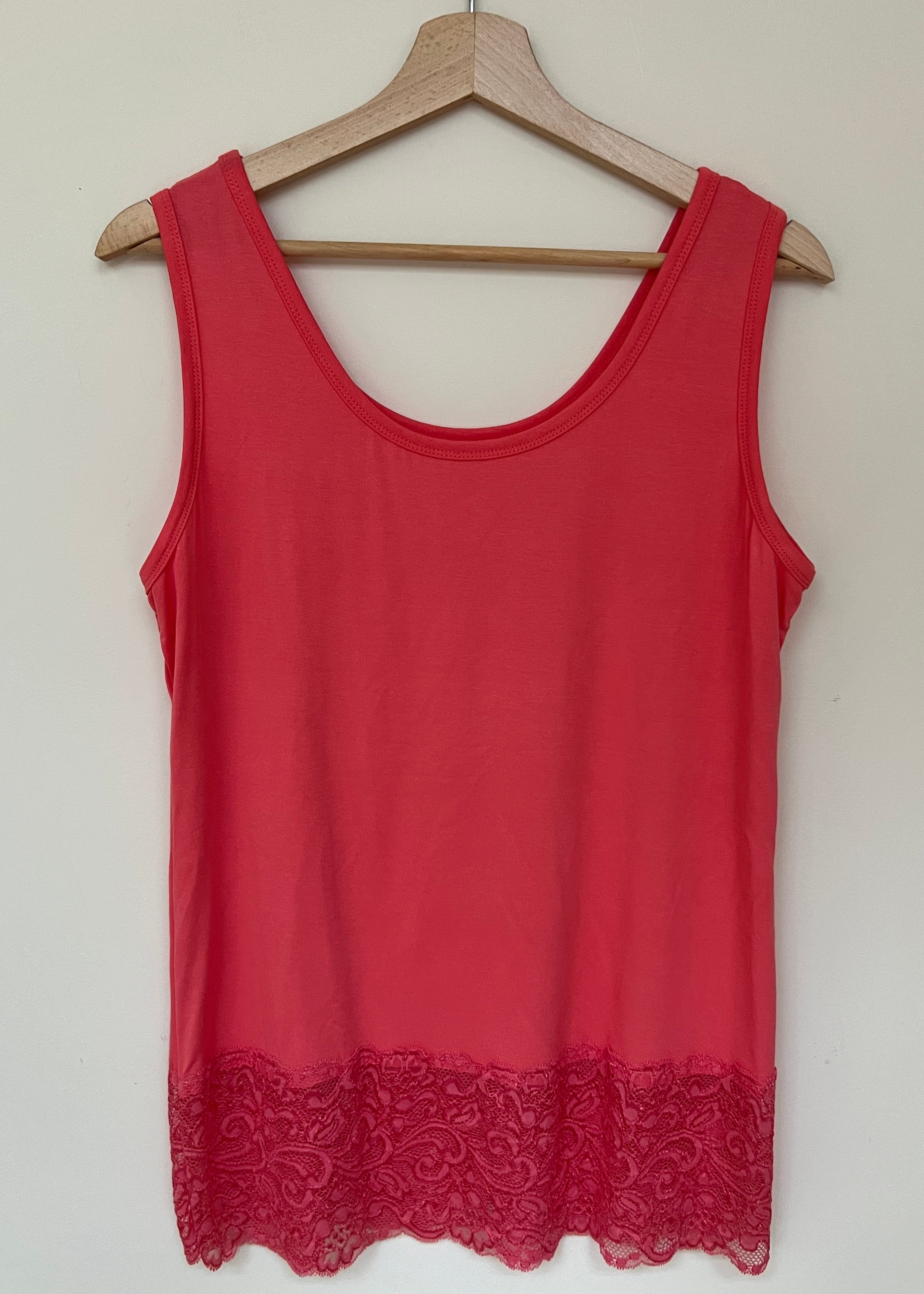 A woman wearing a pink sleeveless vest with a lace hem, paired with blue jeans.