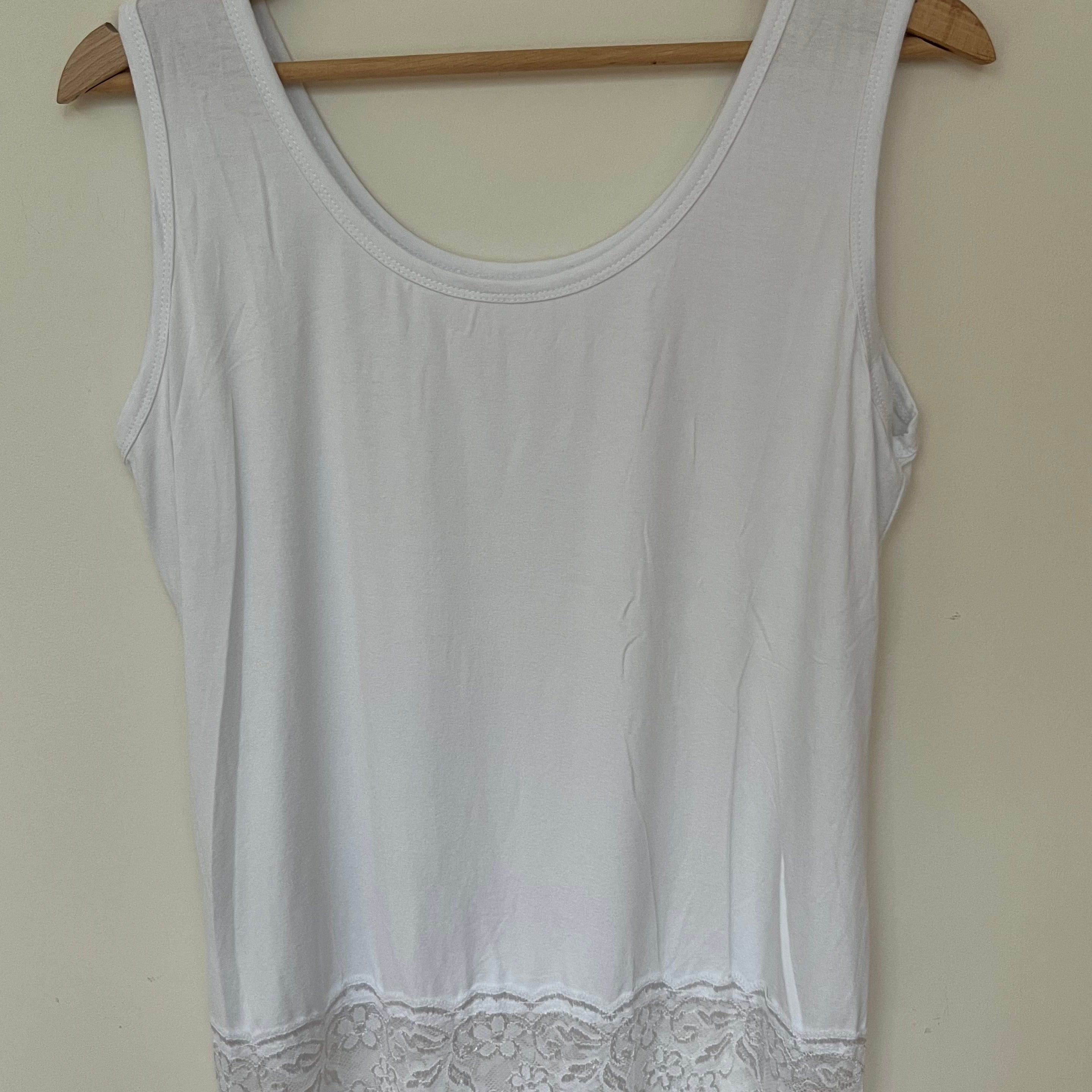 A woman wearing a pink sleeveless vest with a lace hem, paired with blue jeans.