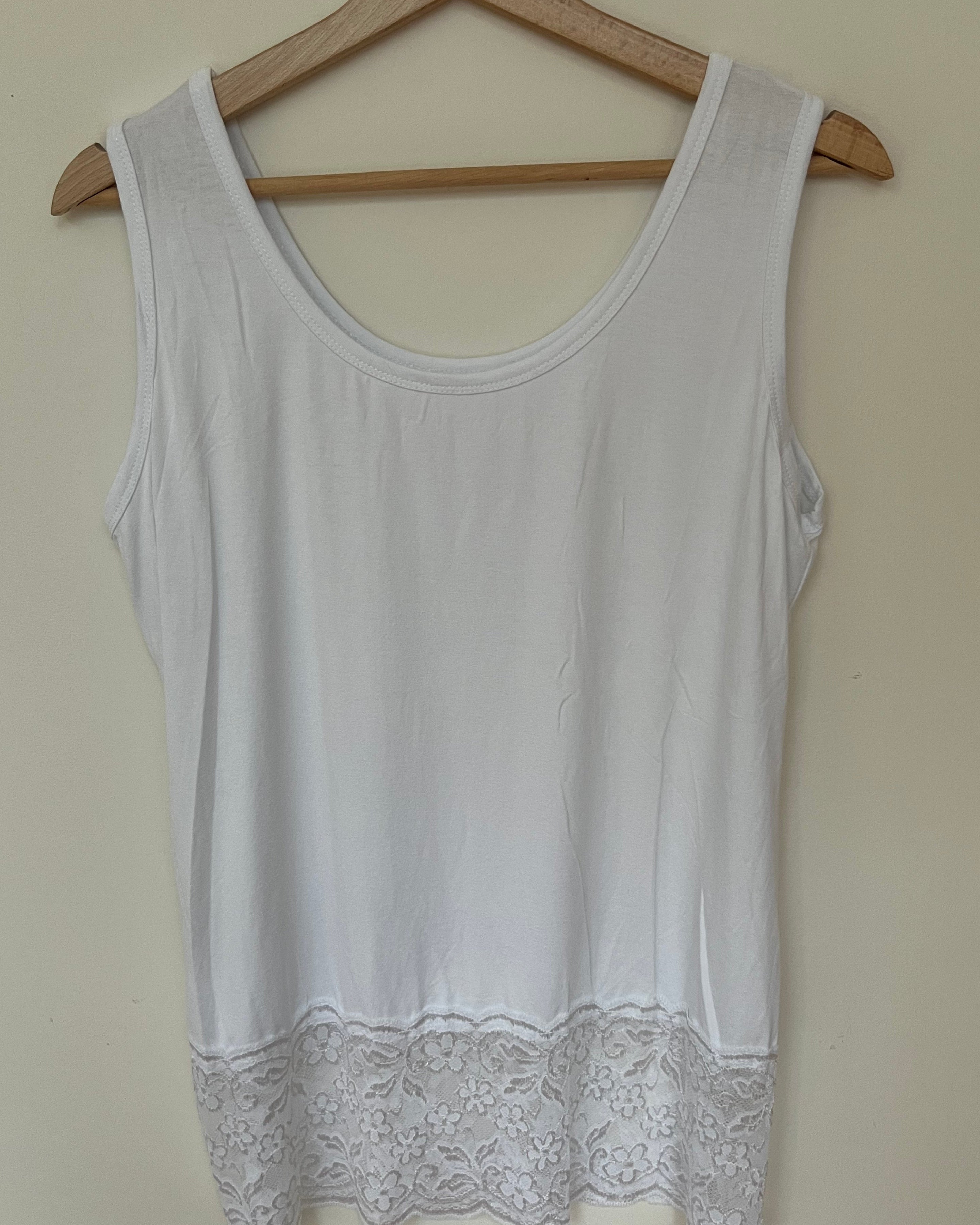 A woman wearing a pink sleeveless vest with a lace hem, paired with blue jeans.