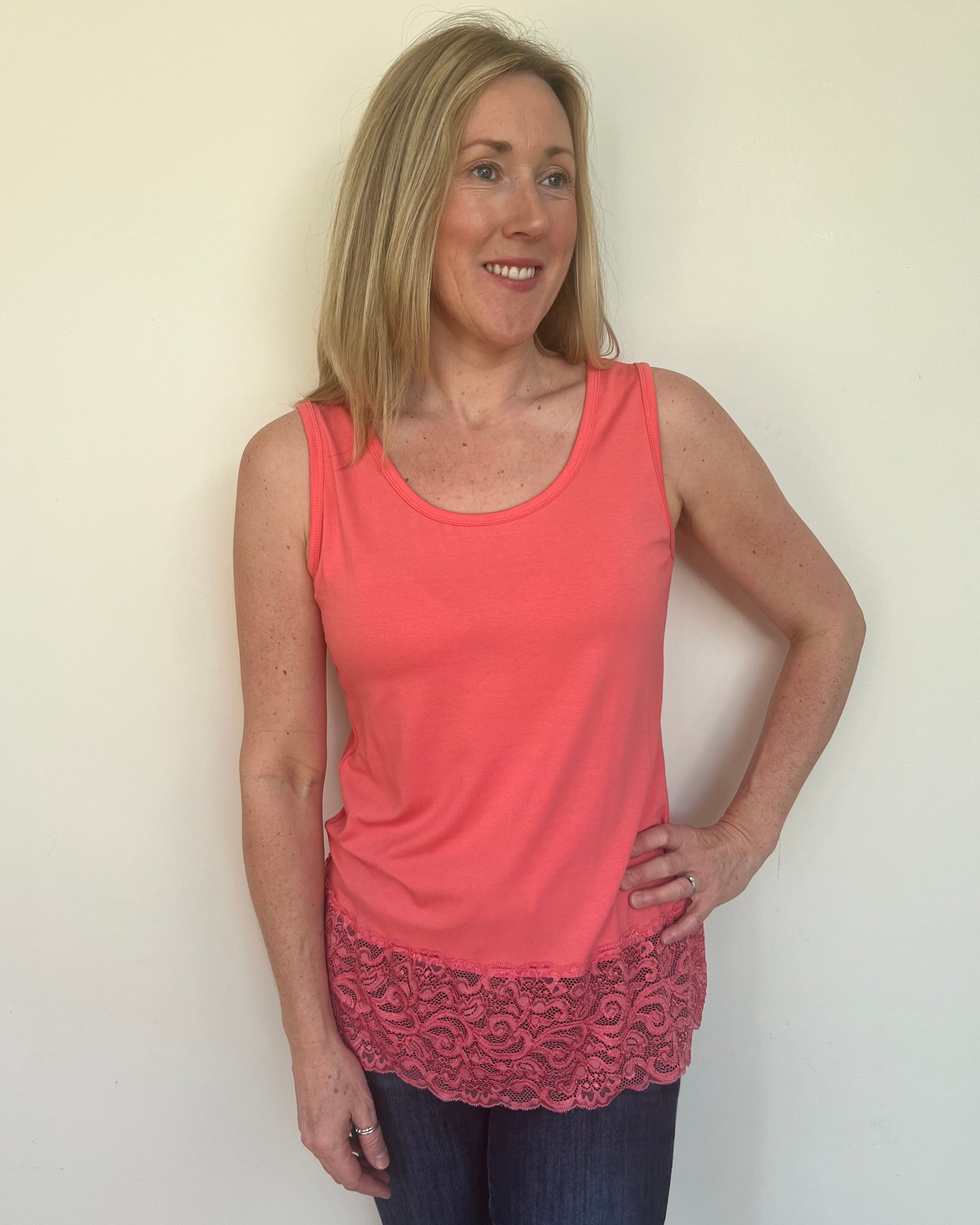A woman wearing a pink sleeveless vest with a lace hem, paired with blue jeans.