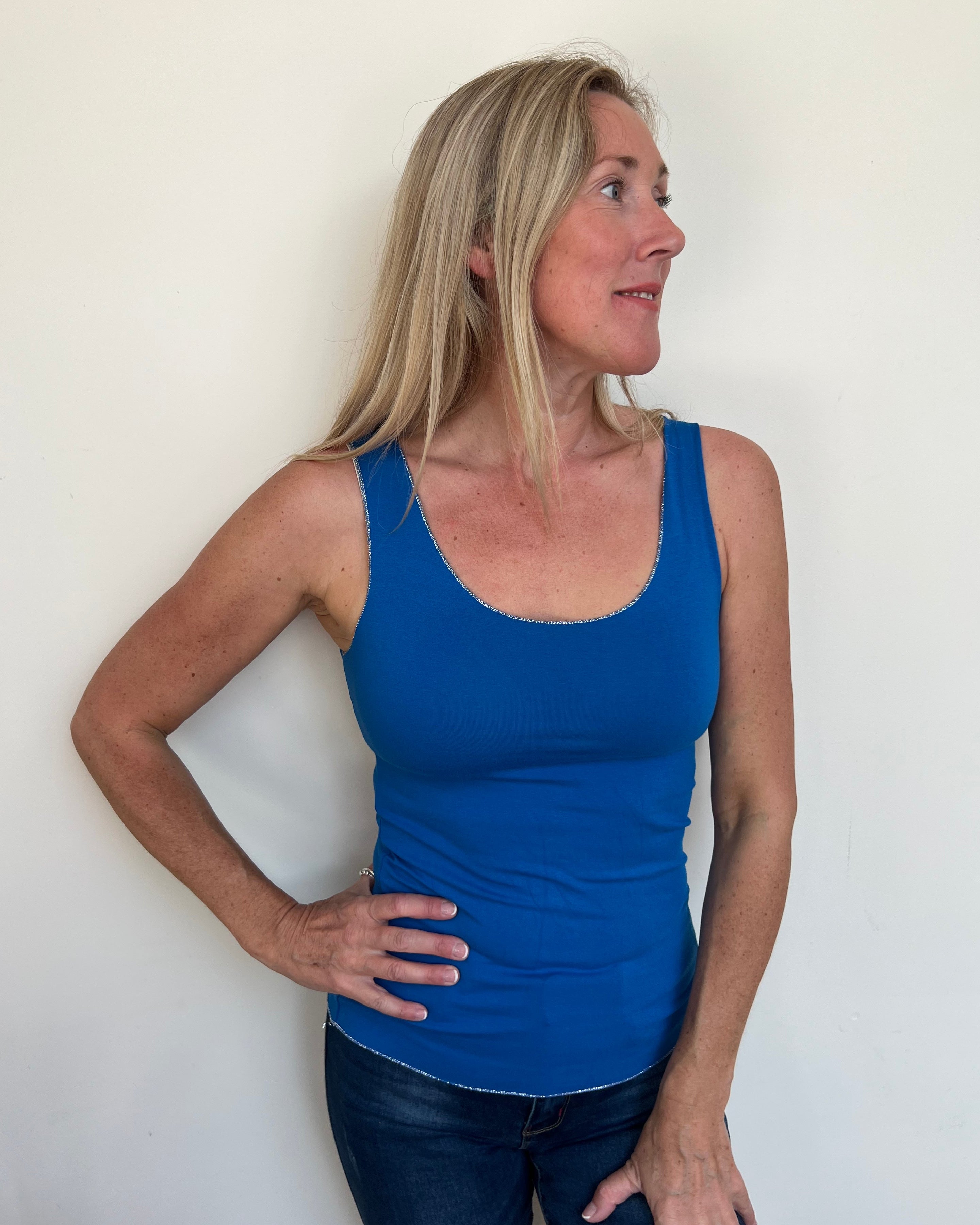 A woman wearing a blue sleeveless tank top, which is the Strati Sparkly Vest, paired with jeans.