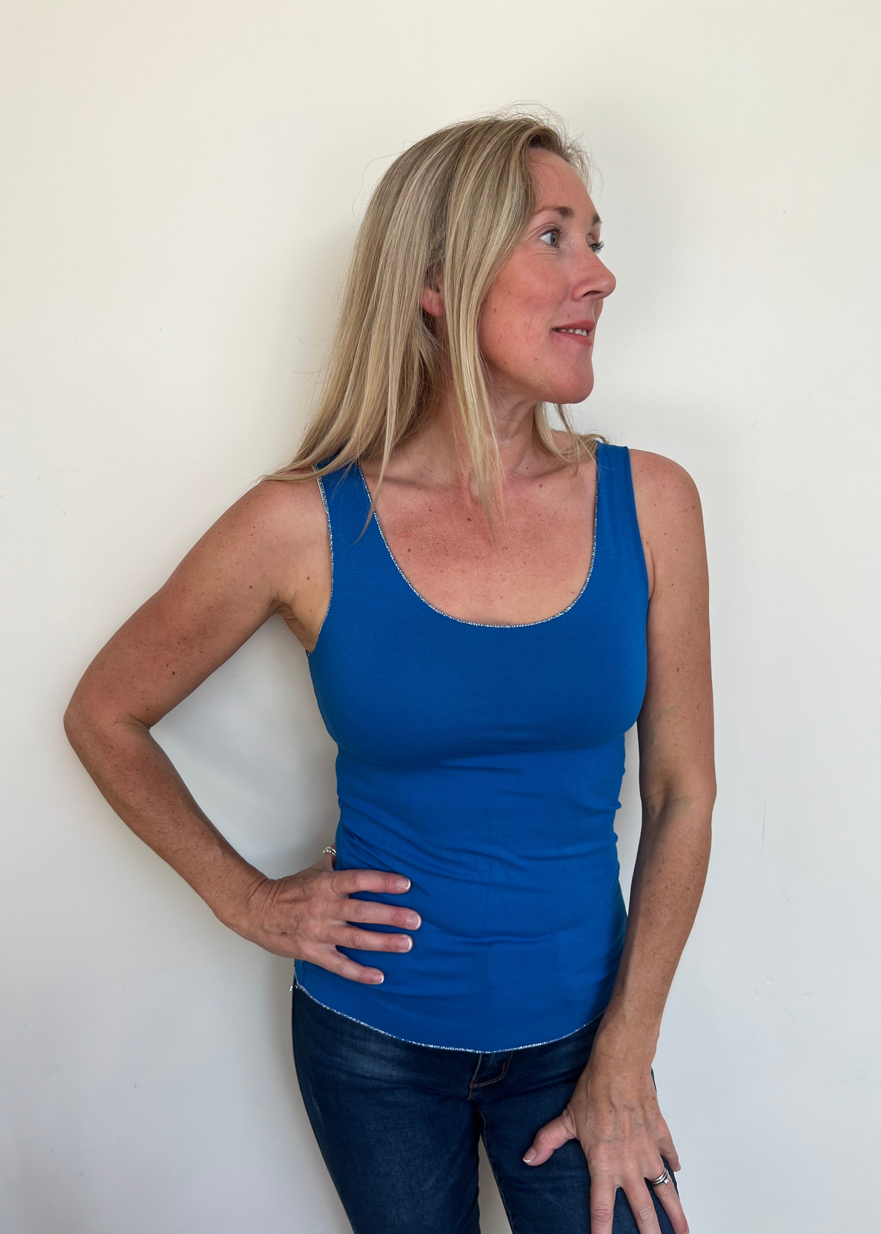 A woman wearing a blue sleeveless tank top, which is the Strati Sparkly Vest, paired with jeans.