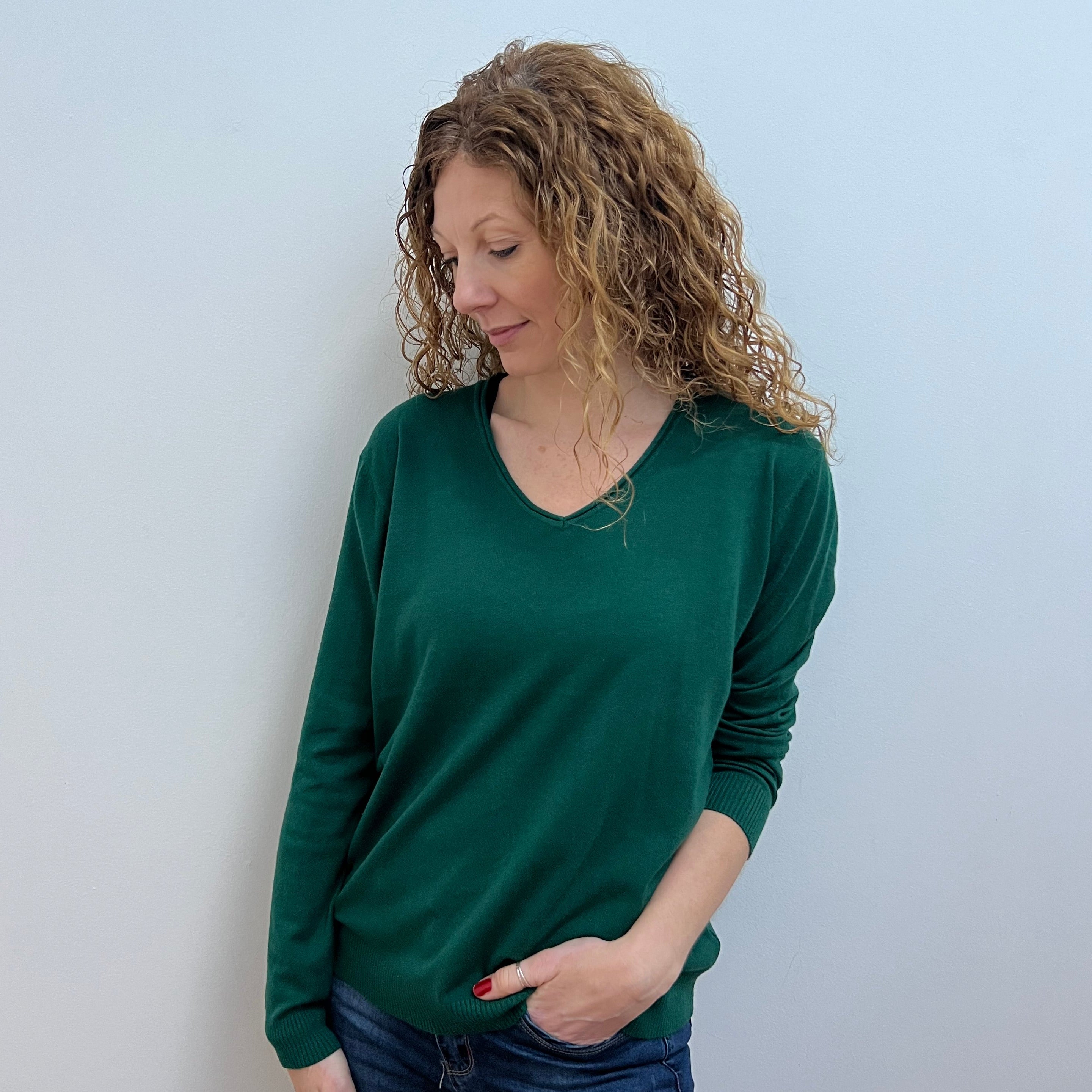 A woman wearing a green V-neck jumper and blue jeans.