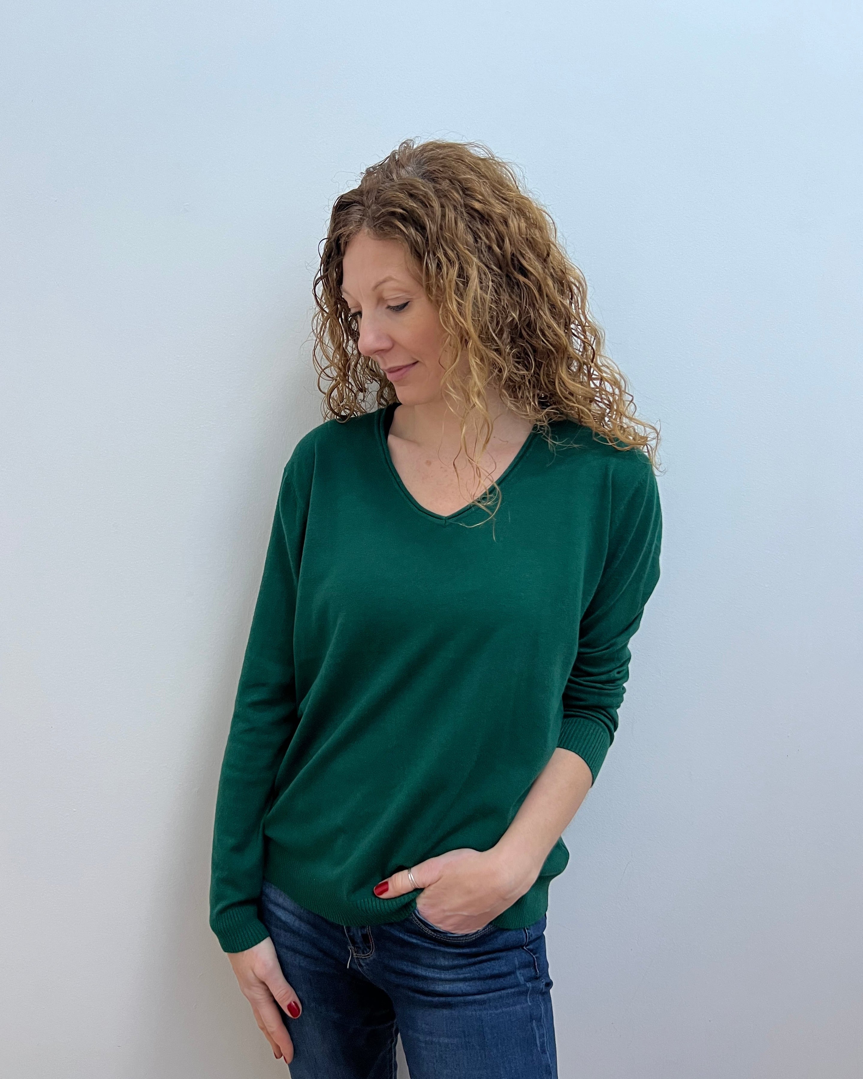 A woman wearing a green V-neck jumper and blue jeans.