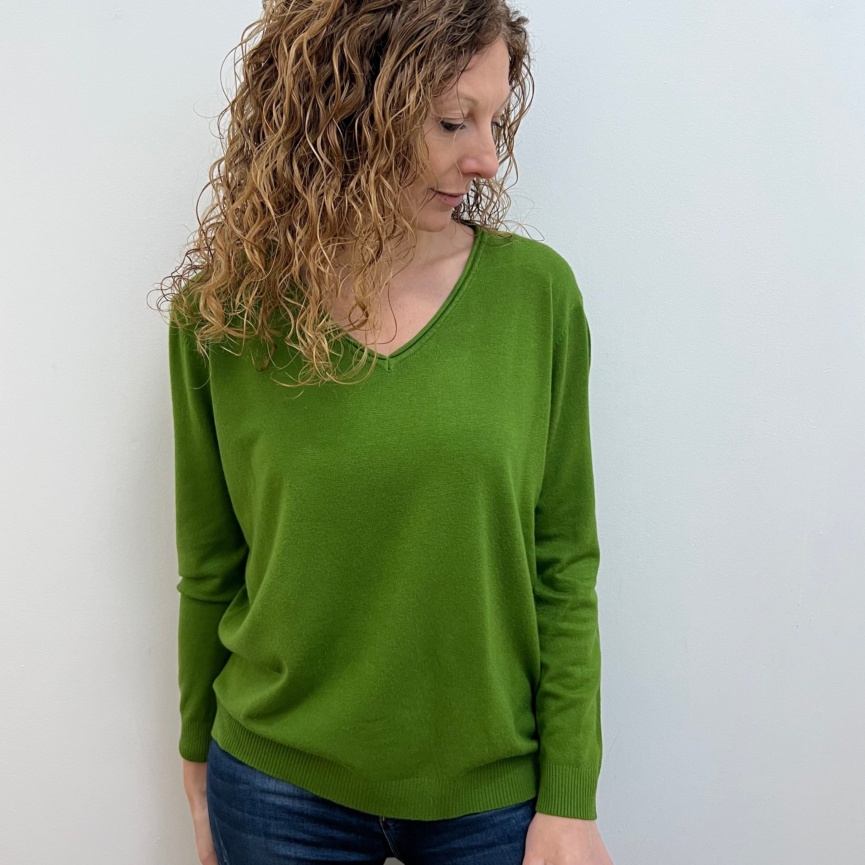 A woman wearing a green wide v neck jumper in a casual setting, with the jumper fitting comfortably.