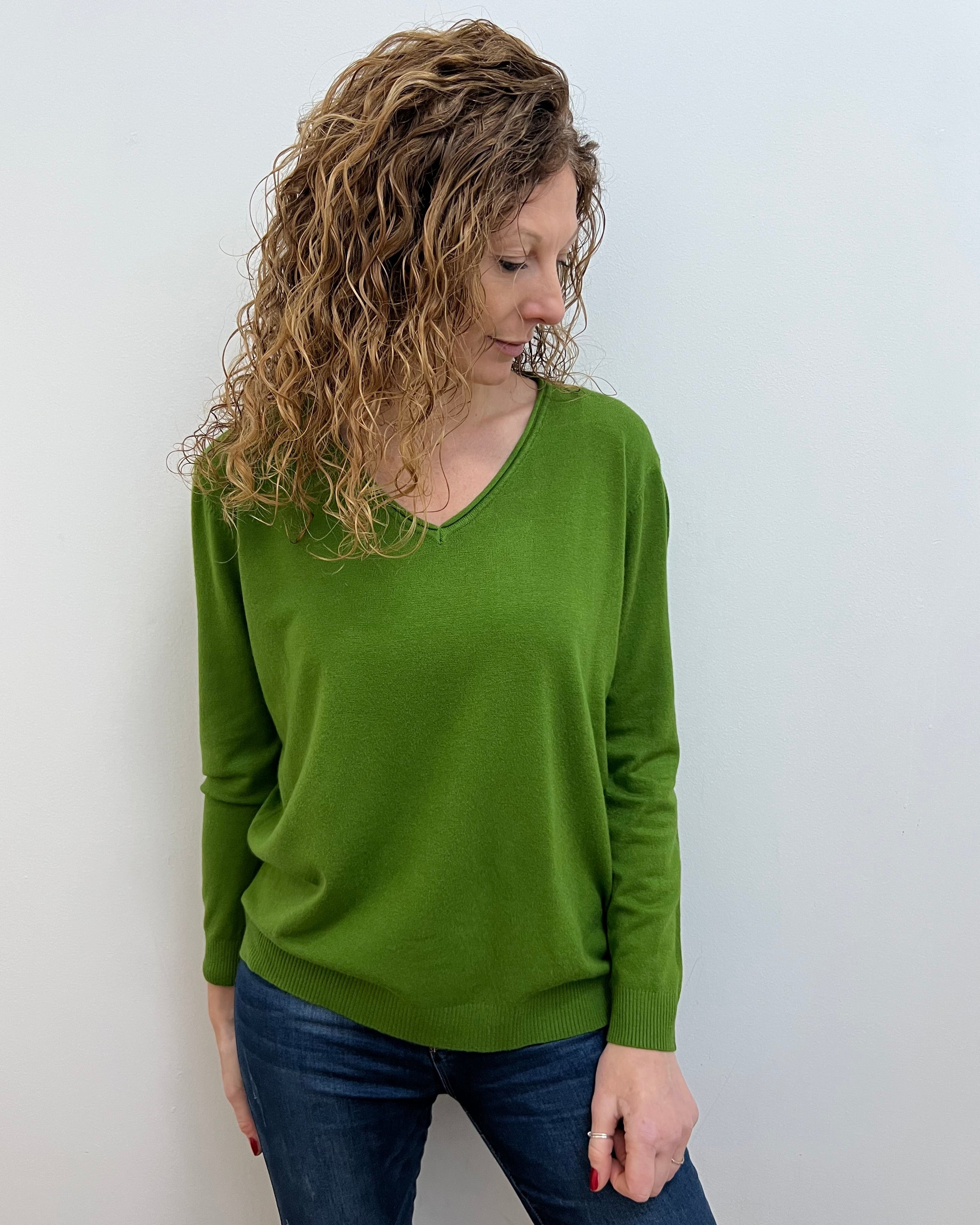 A woman wearing a green wide v neck jumper in a casual setting, with the jumper fitting comfortably.