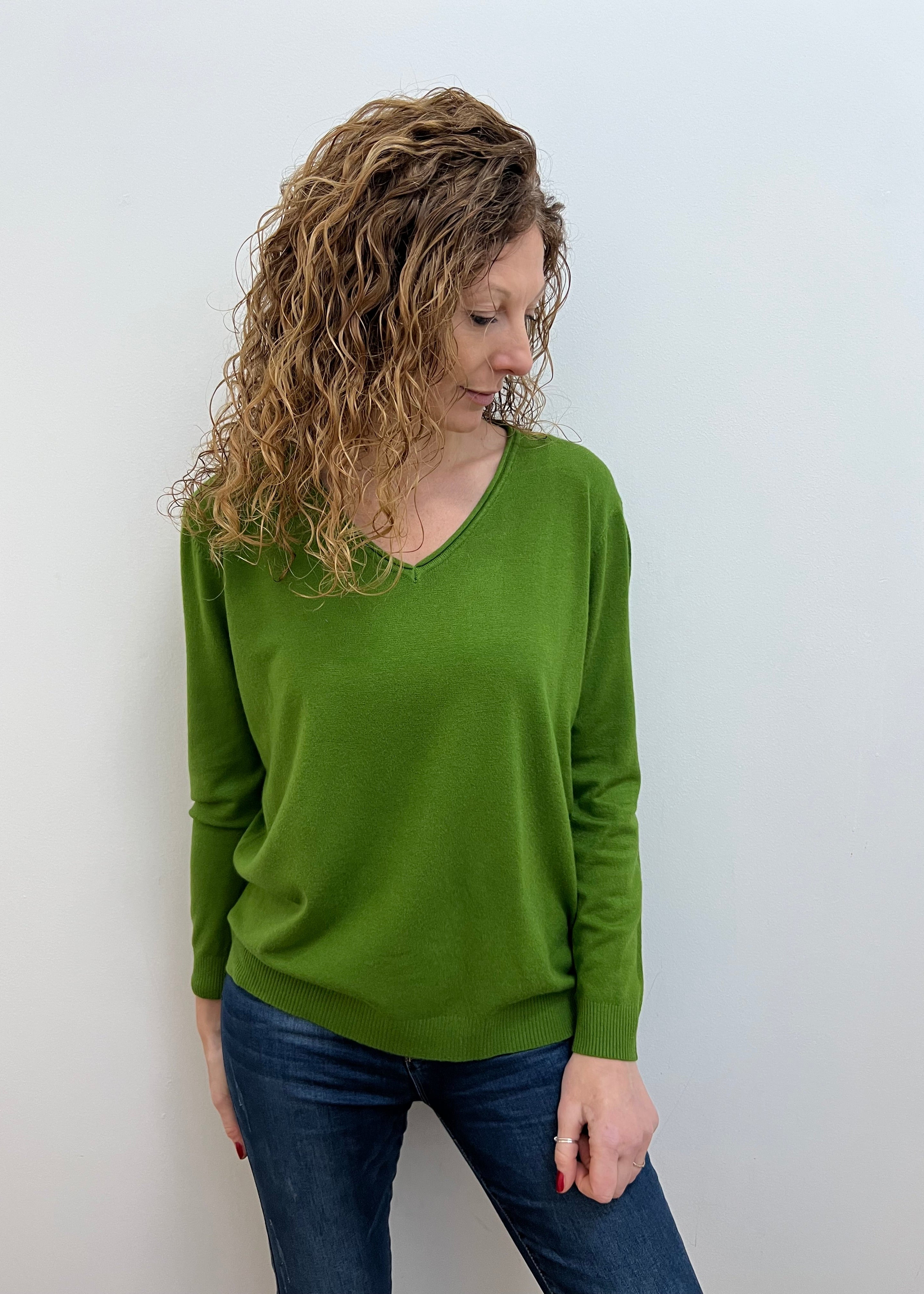 A woman wearing a green wide v neck jumper in a casual setting, with the jumper fitting comfortably.