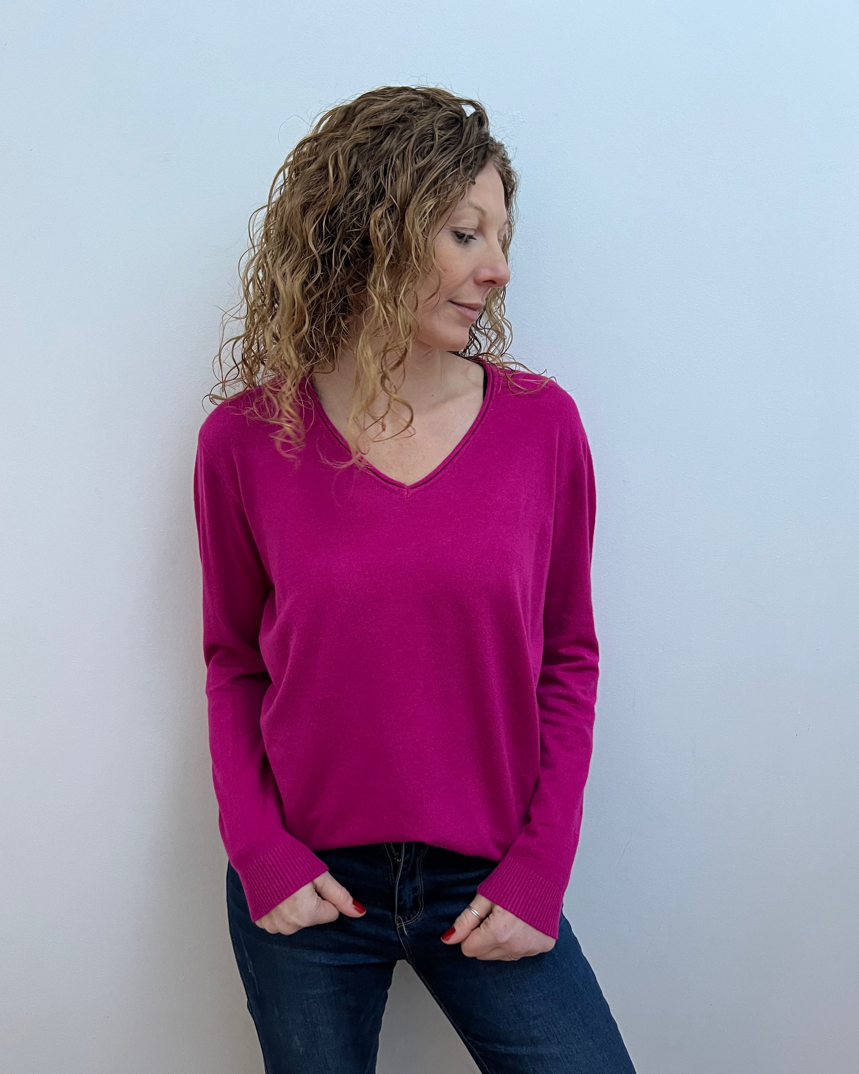 A woman wearing a pink V-neck jumper and blue jeans.