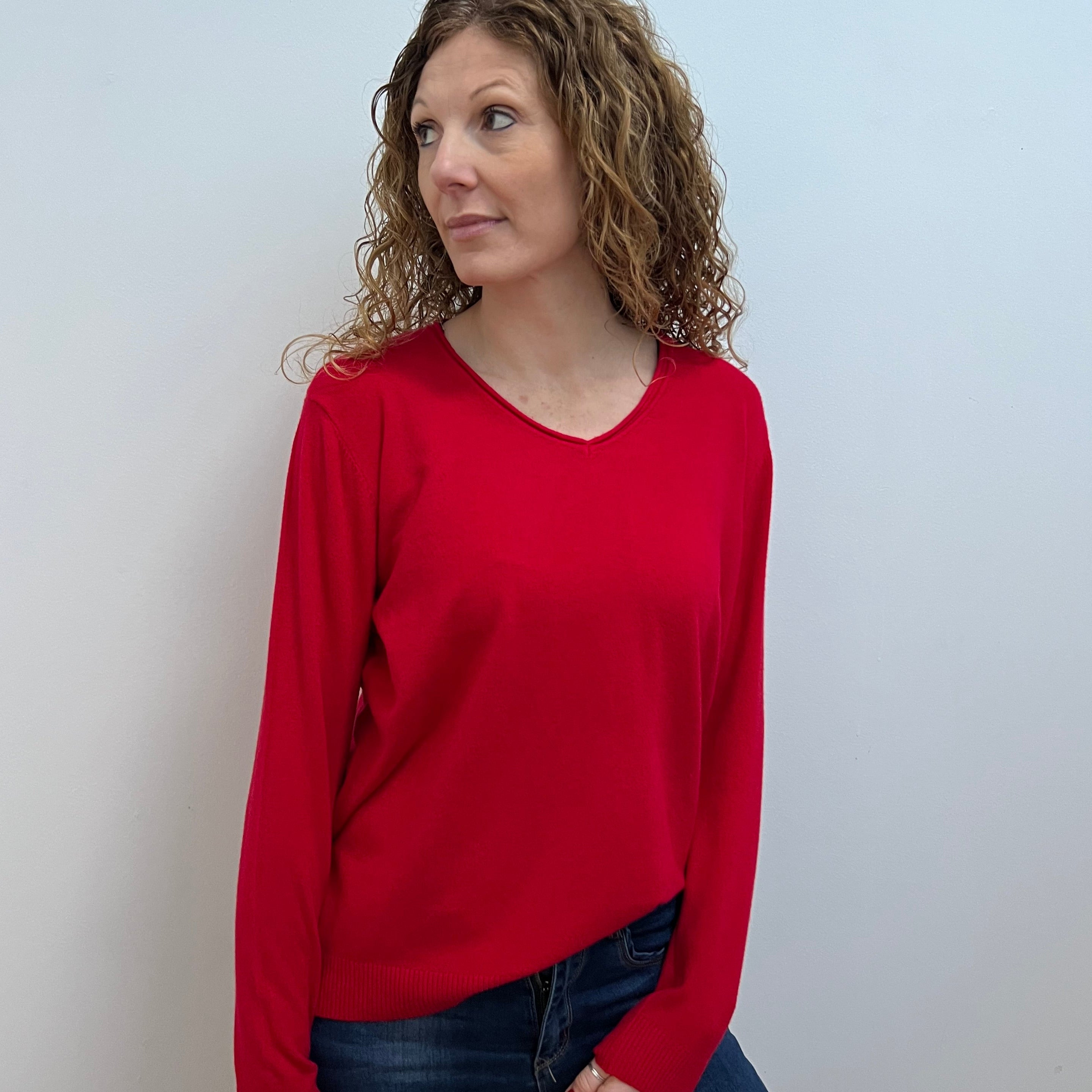 A woman wearing a red V-neck jumper and blue jeans.