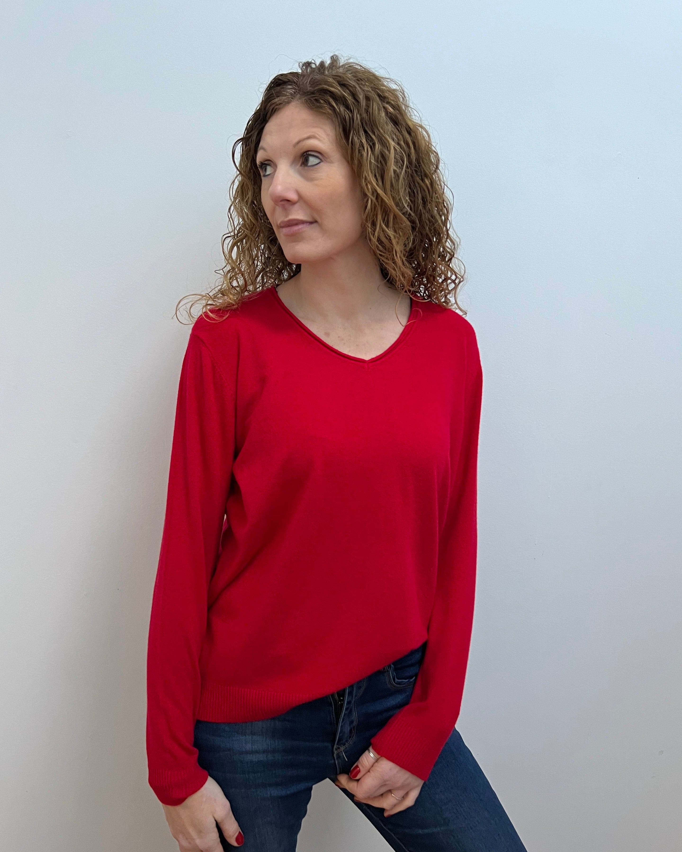 A woman wearing a red V-neck jumper and blue jeans.